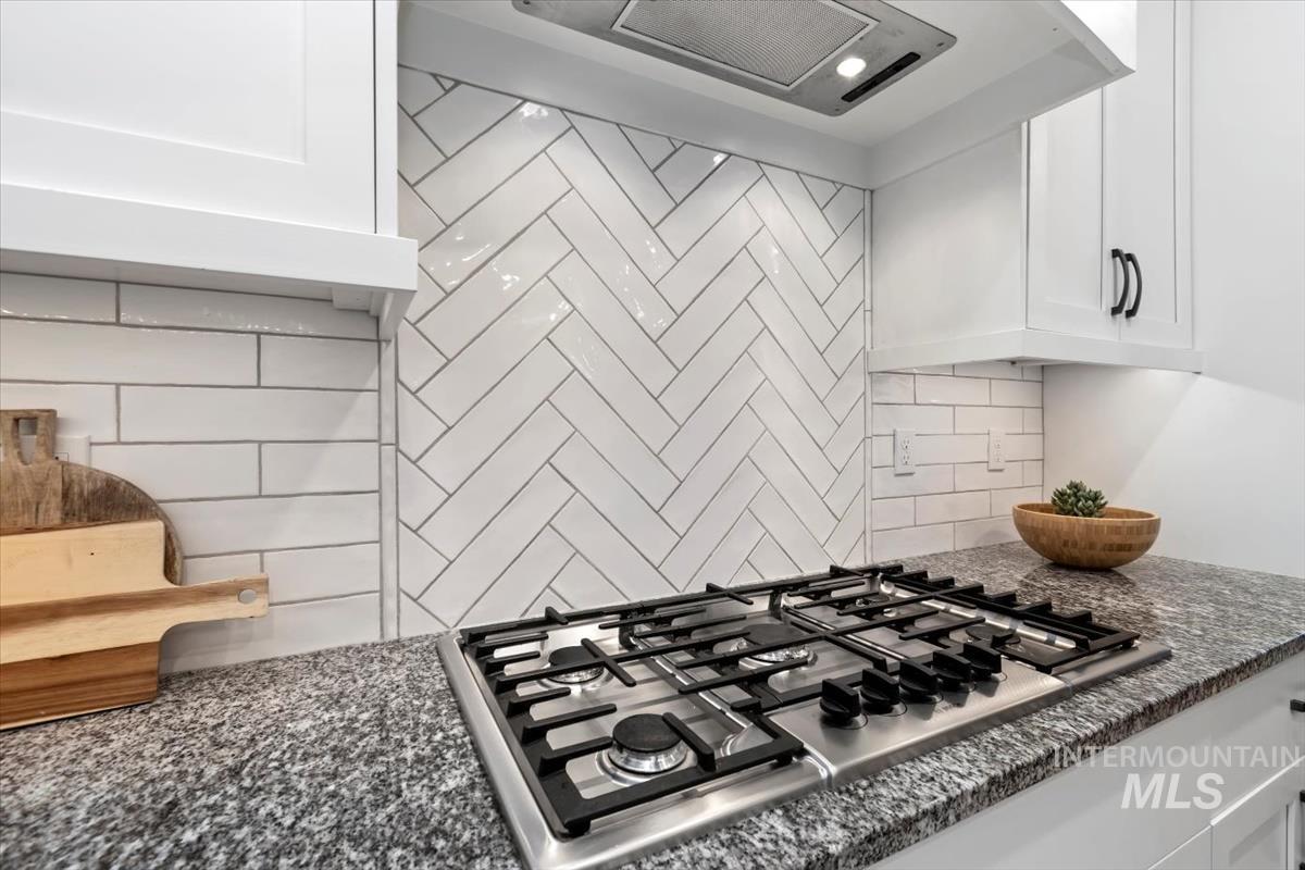 Kitchen featuring stainless steel gas cooktop, extractor fan, white cabinetry, decorative backsplash, and dark stone counters