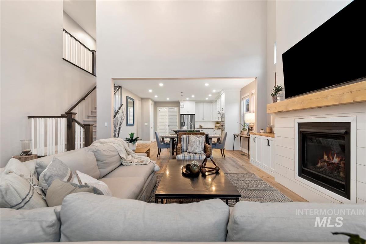 Living area with recessed lighting, light wood finished floors, stairway, a glass covered fireplace, and a towering ceiling