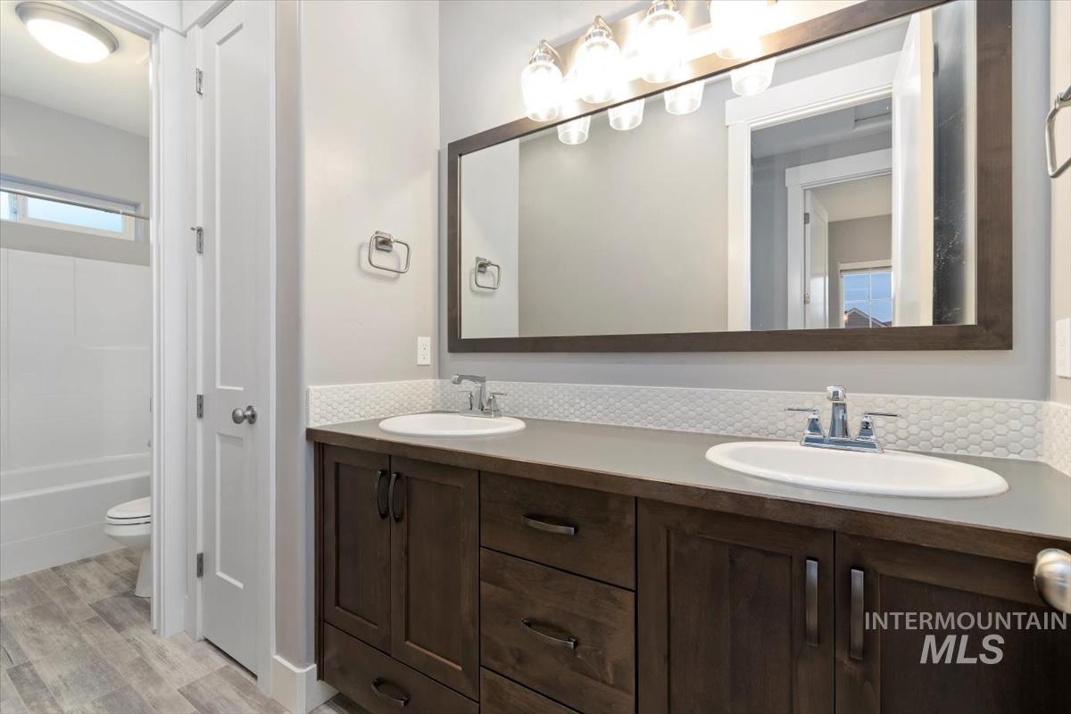 Full bath featuring double vanity, light wood finished floors, and shower / bath combination