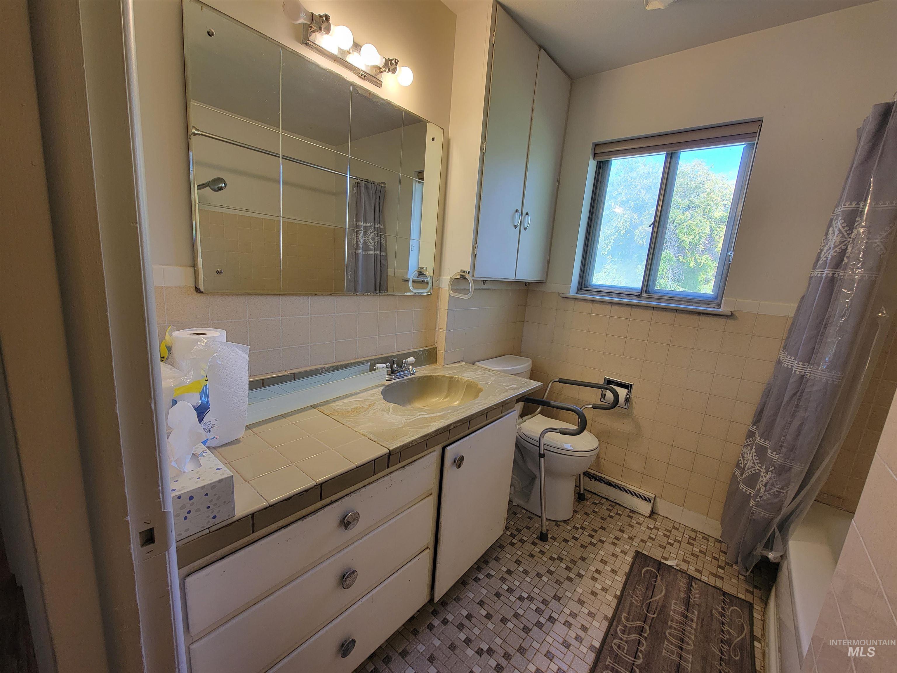 Full bathroom featuring vanity, a baseboard radiator, tile patterned floors, tile walls, and shower / tub combo