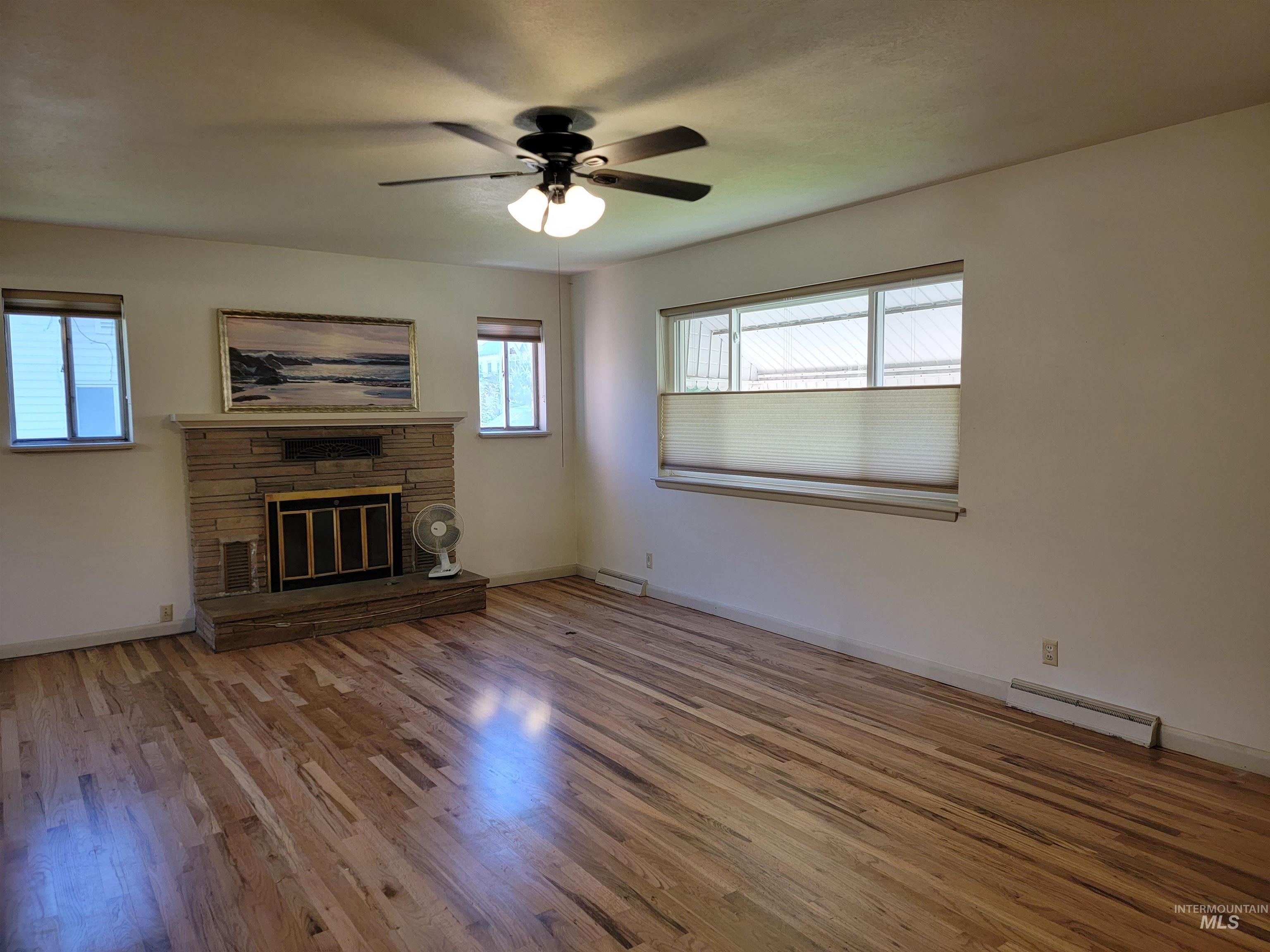 Unfurnished living room with light wood-style floors, a stone fireplace, a ceiling fan, and a baseboard heating unit