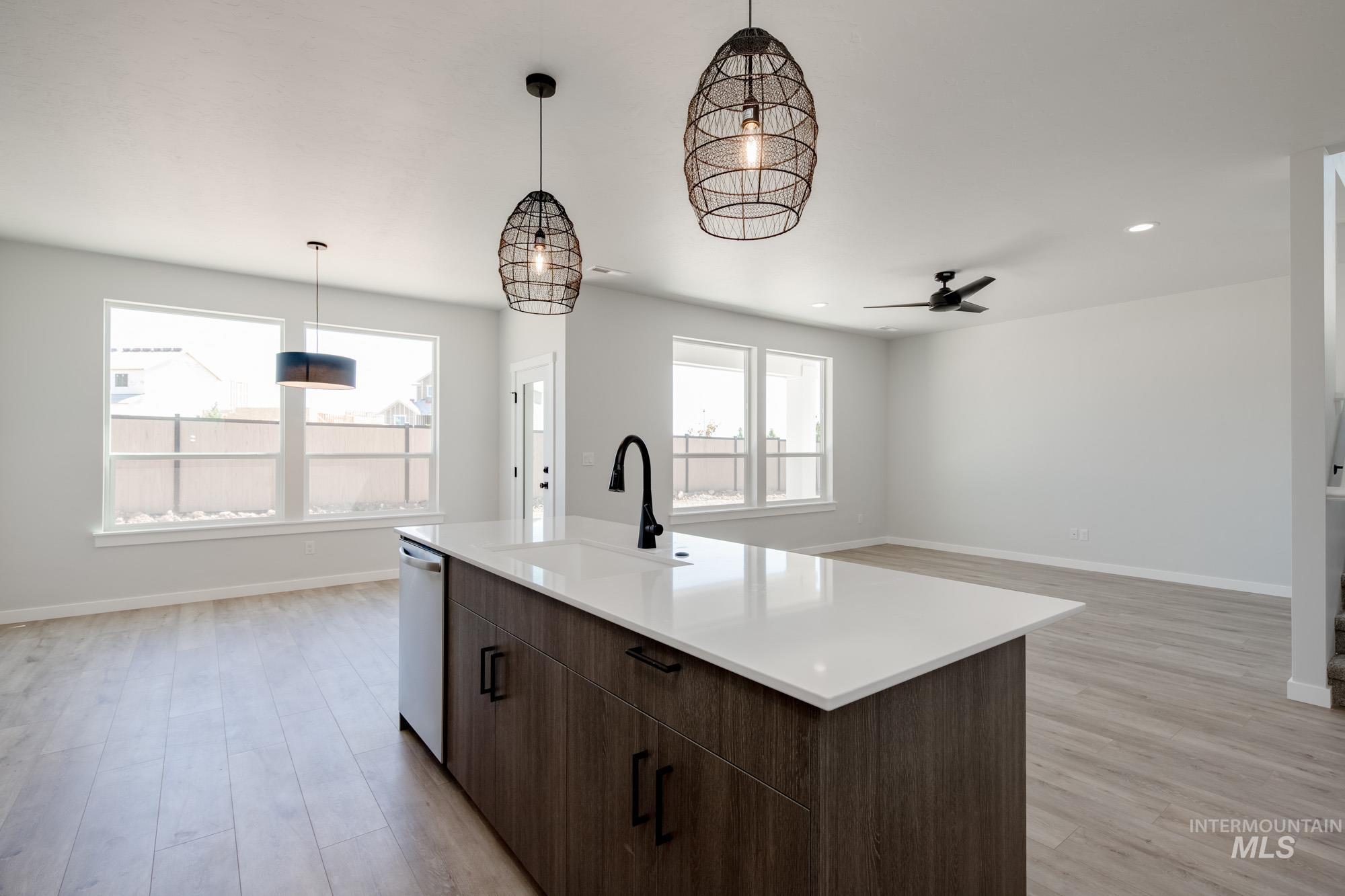 Kitchen with dishwasher, light wood-style floors, a ceiling fan, light countertops, and hanging light fixtures