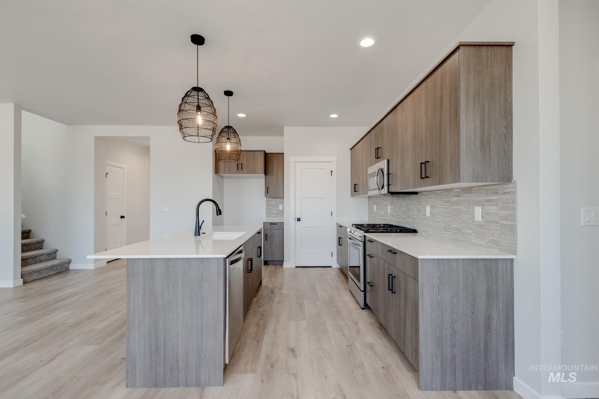 Kitchen with stainless steel appliances, decorative backsplash, light countertops, light wood-type flooring, and hanging light fixtures