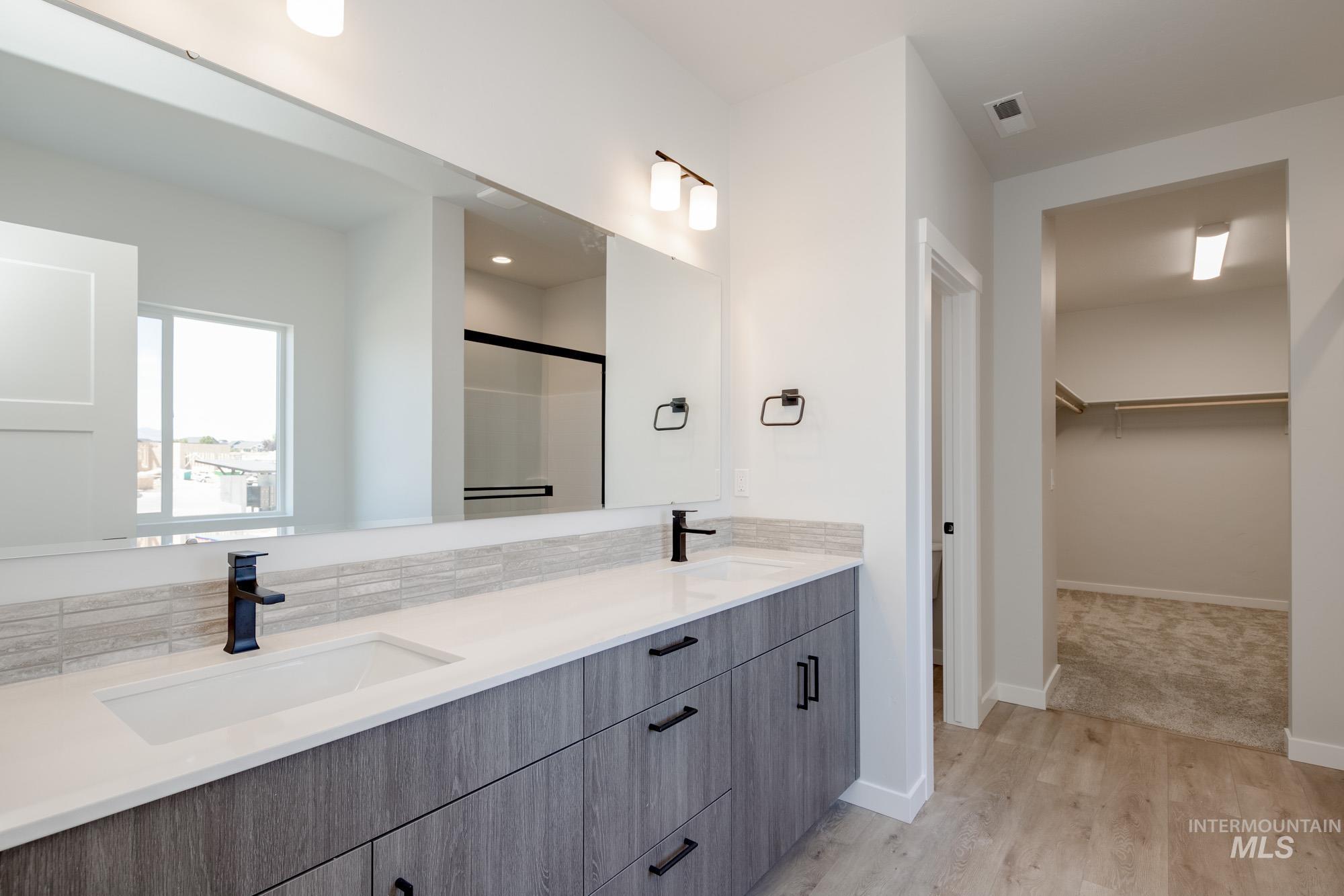 Bathroom with double vanity, a walk in closet, wood finished floors, decorative backsplash, and a shower with door