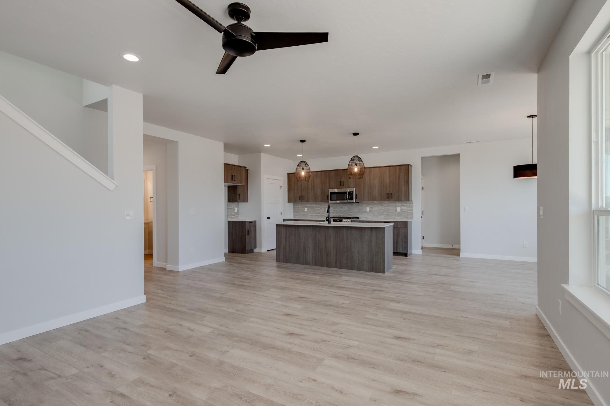 Kitchen featuring stainless steel microwave, open floor plan, decorative backsplash, light countertops, and recessed lighting