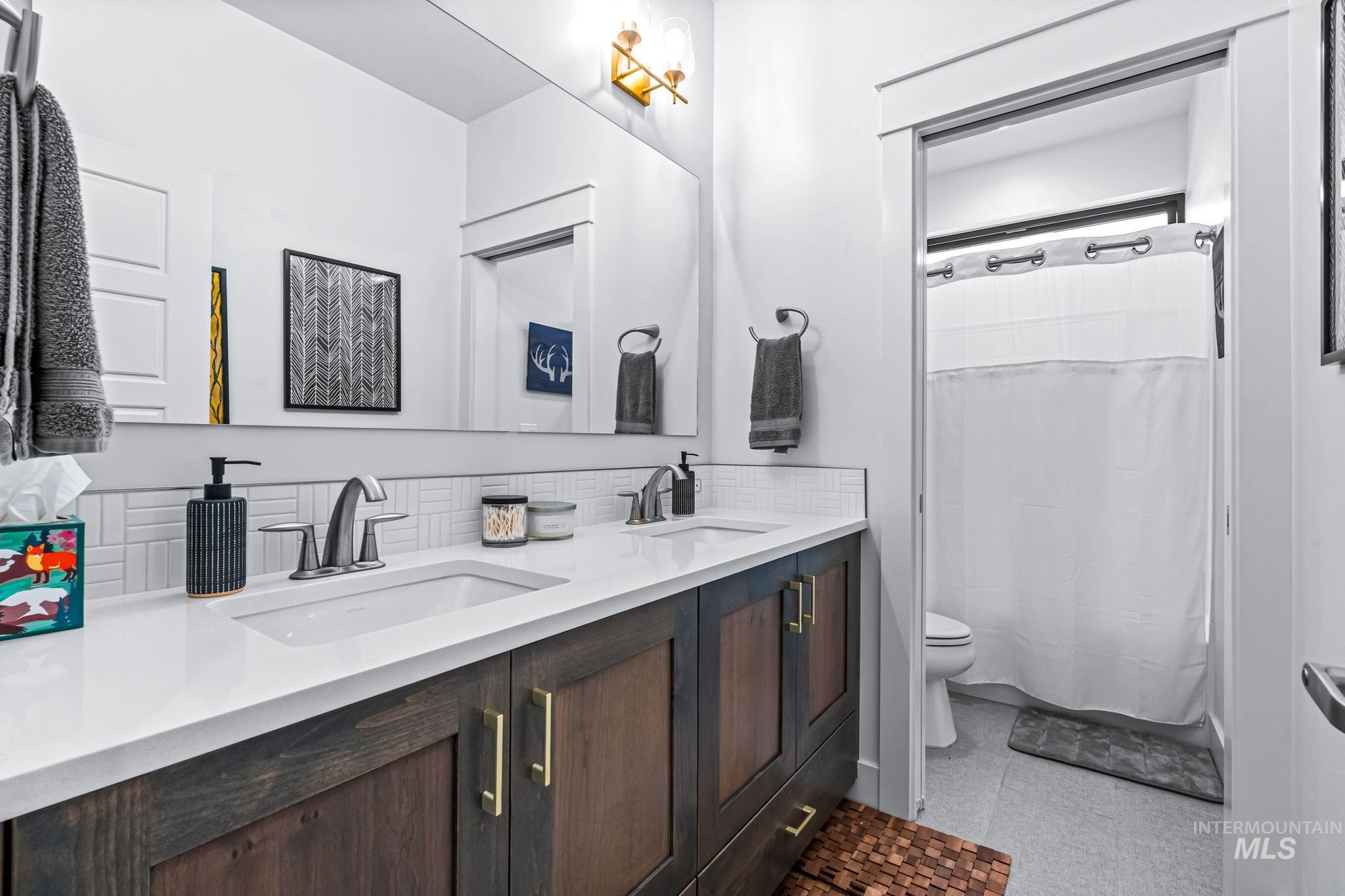 Full bathroom featuring double vanity, a shower with shower curtain, and tasteful backsplash