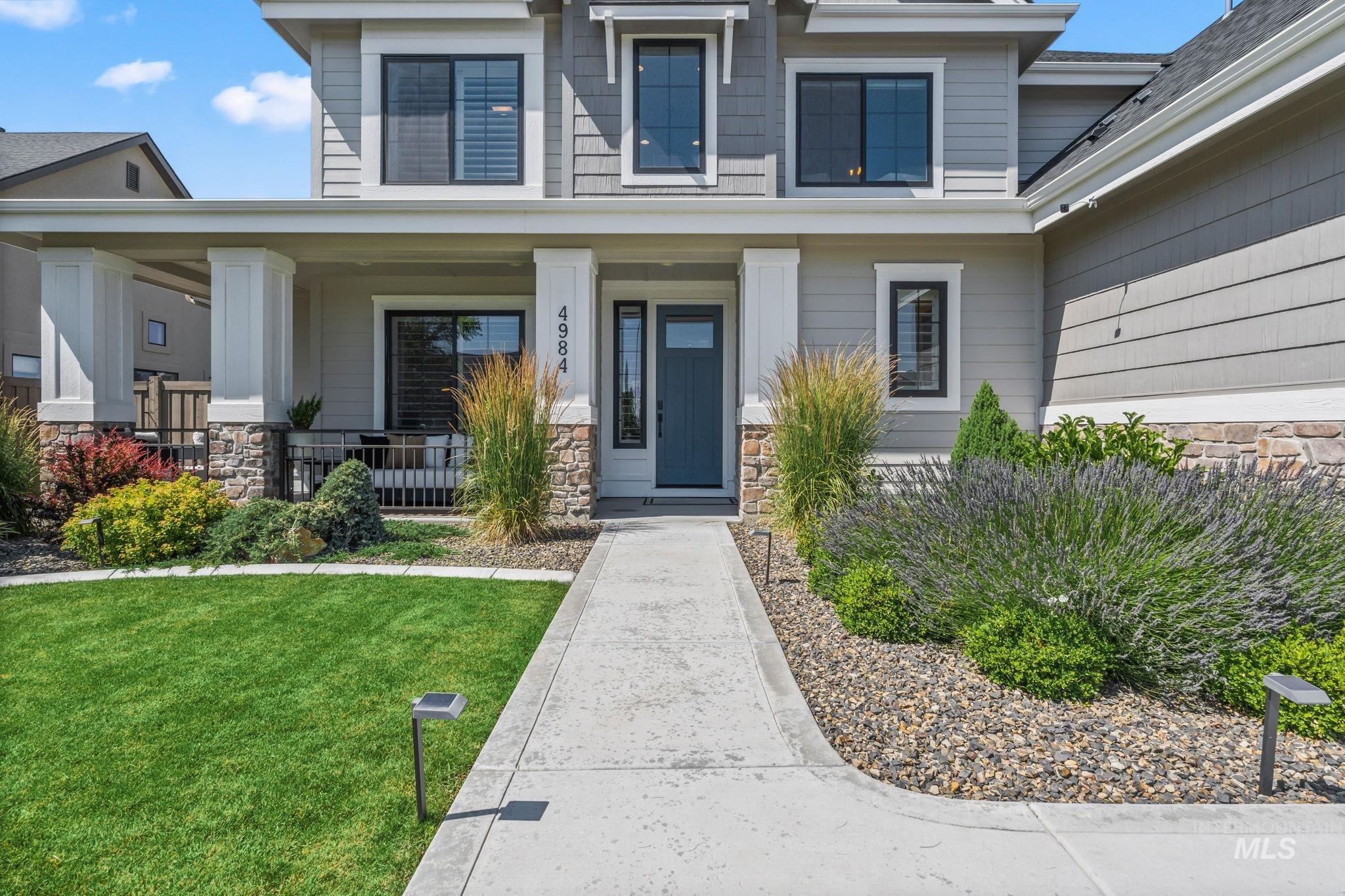 View of exterior entry featuring stone siding, covered porch, and a yard