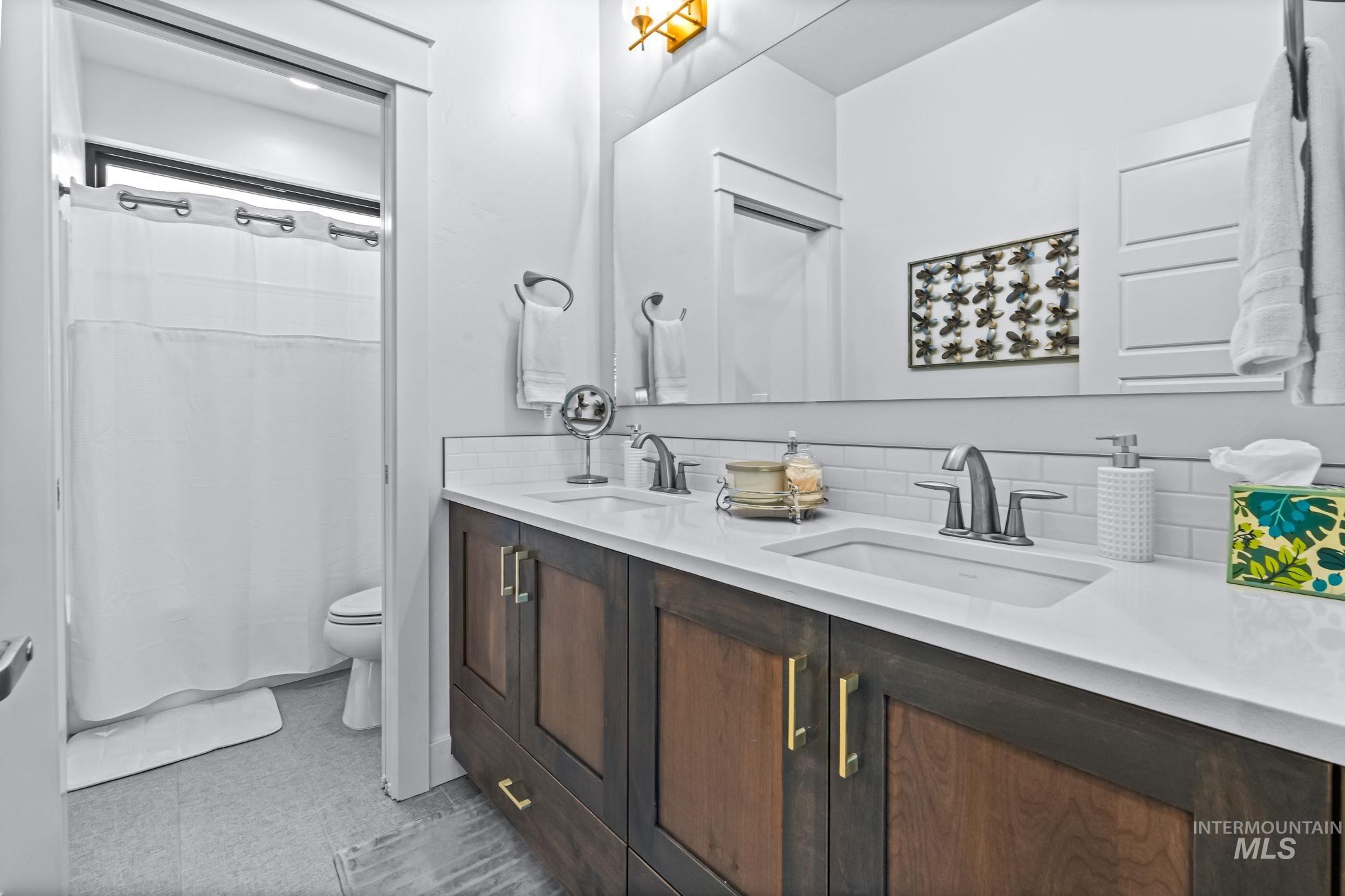Bathroom with double vanity, a shower with shower curtain, and tasteful backsplash