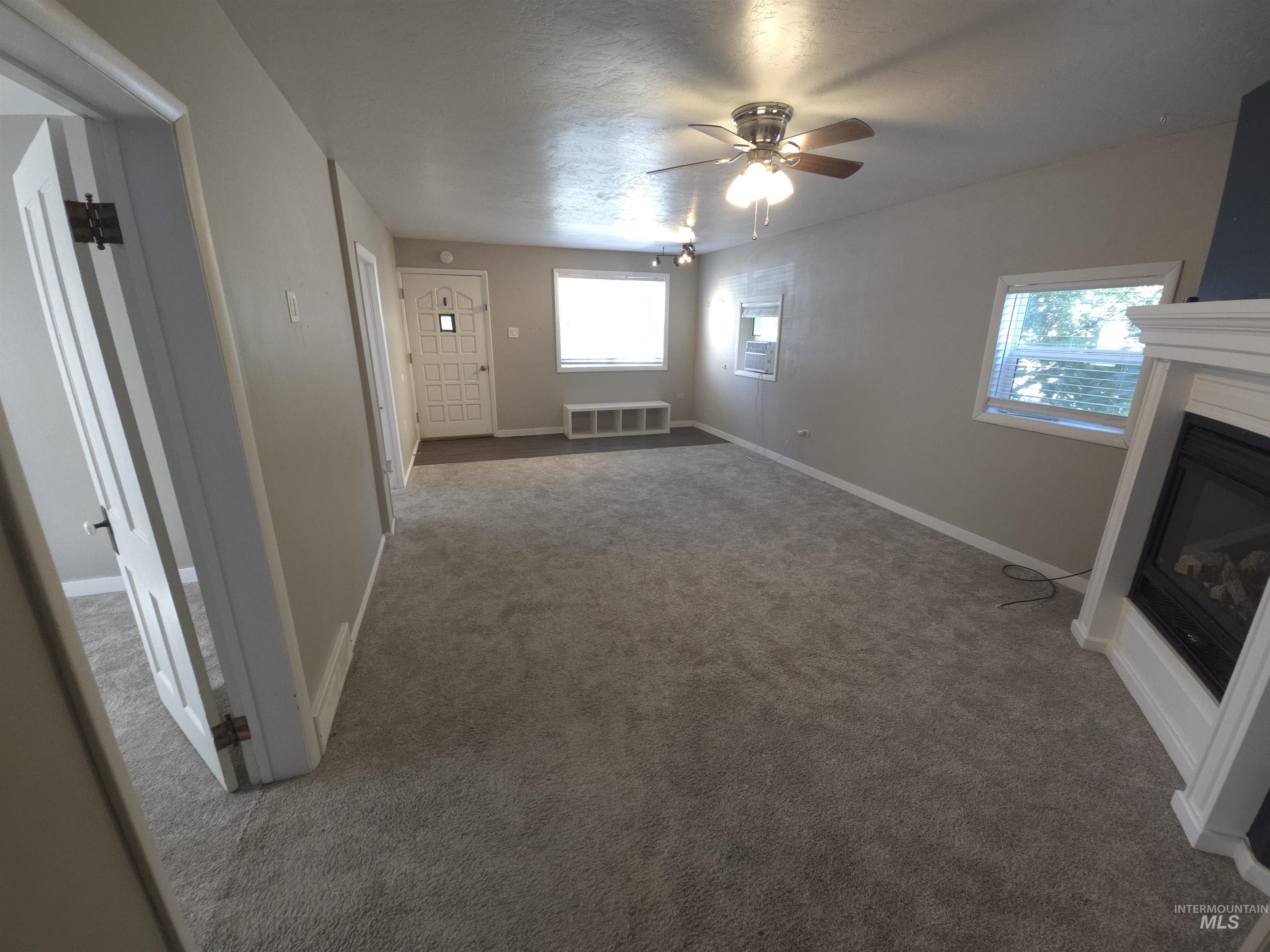 Unfurnished living room with a glass covered fireplace, carpet, and a ceiling fan