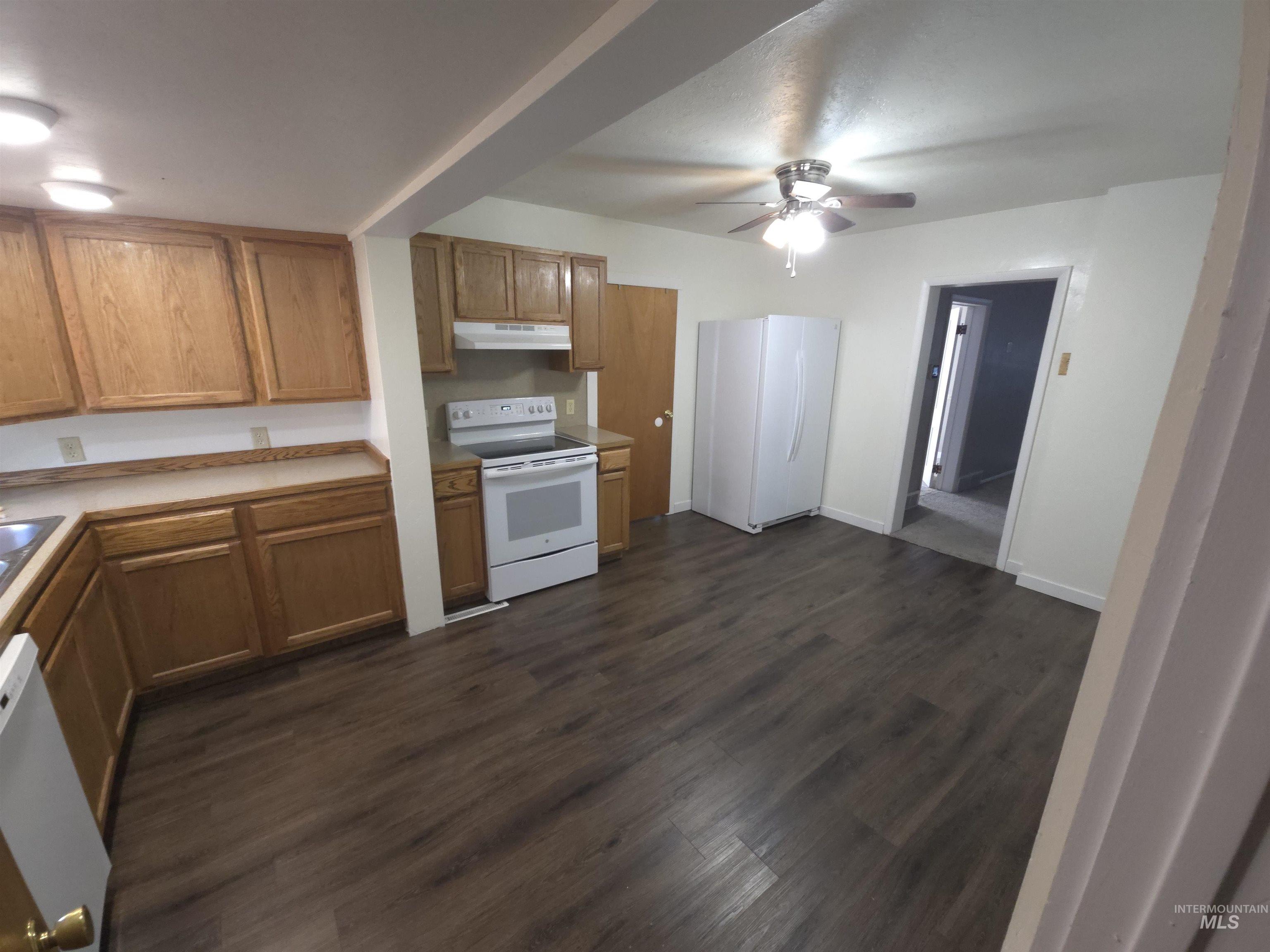 Kitchen with white appliances, ceiling fan, light countertops, dark wood-style floors, and under cabinet range hood