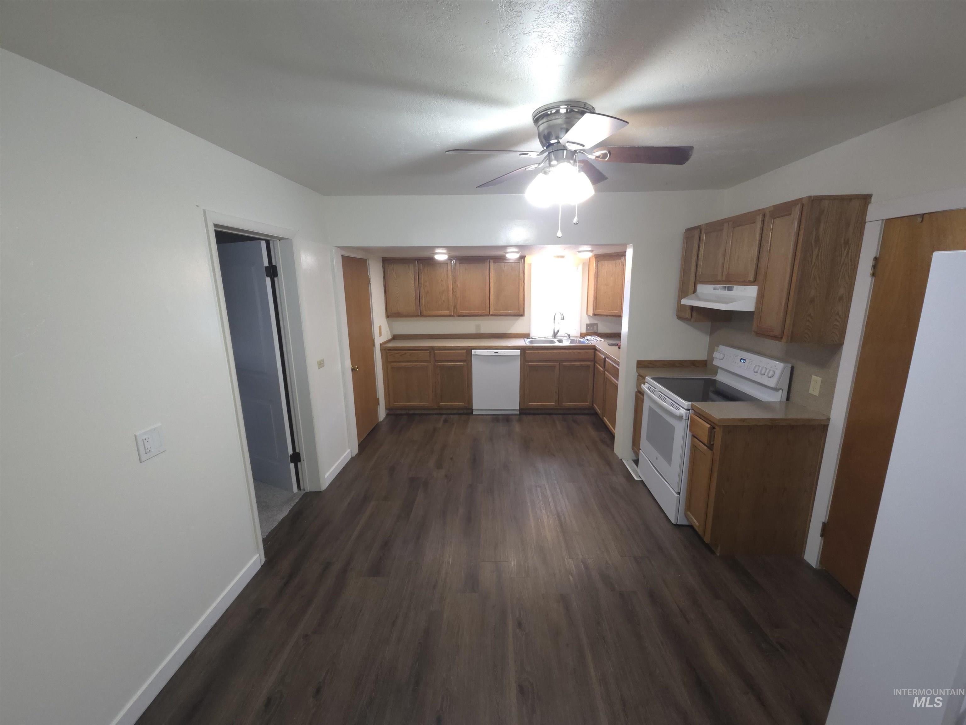 Kitchen with white appliances, dark wood finished floors, a ceiling fan, light countertops, and under cabinet range hood