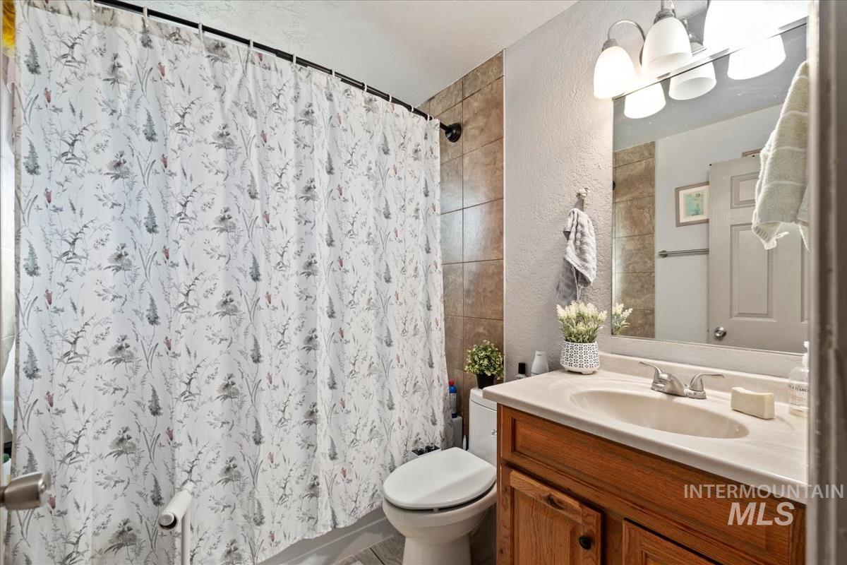 Bathroom featuring a textured wall, vanity, and shower / bath combination with curtain