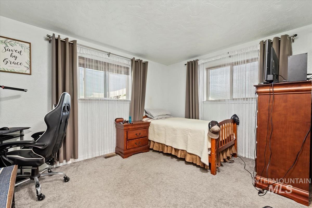 Bedroom featuring light colored carpet, multiple windows, an office area, and a textured ceiling