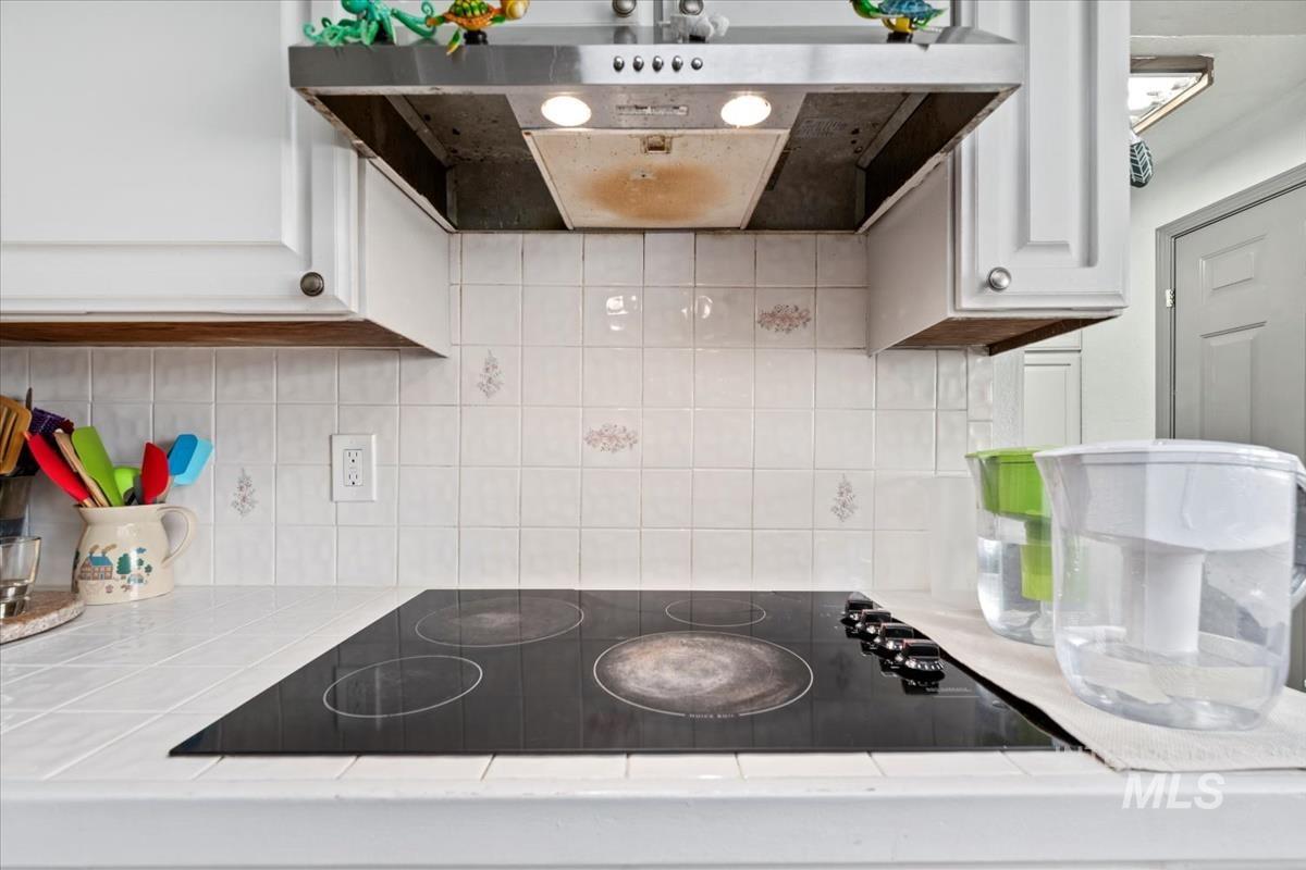 Kitchen featuring under cabinet range hood, black electric stovetop, decorative backsplash, and white cabinets