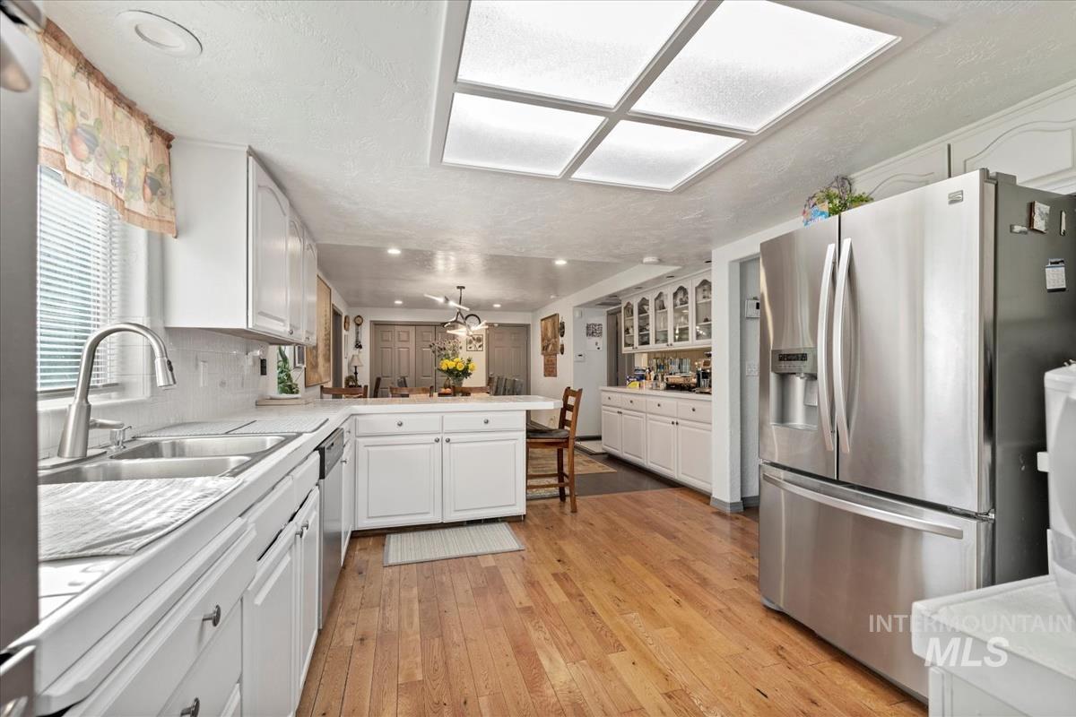 Kitchen featuring appliances with stainless steel finishes, light wood-style flooring, a peninsula, light countertops, and white cabinetry