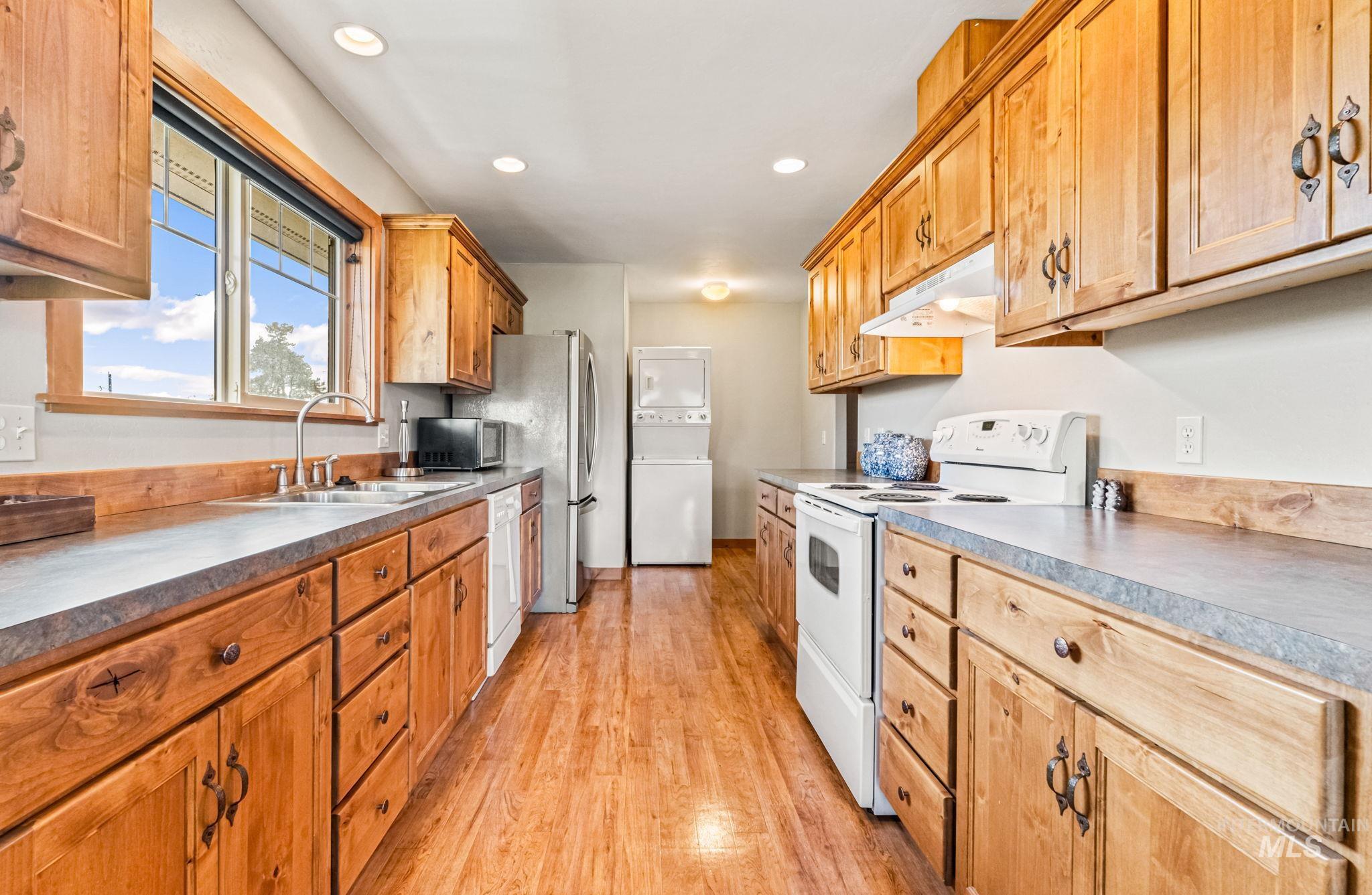 Kitchen with white appliances, light wood-style floors, under cabinet range hood, recessed lighting, and estacked washer and dryer
