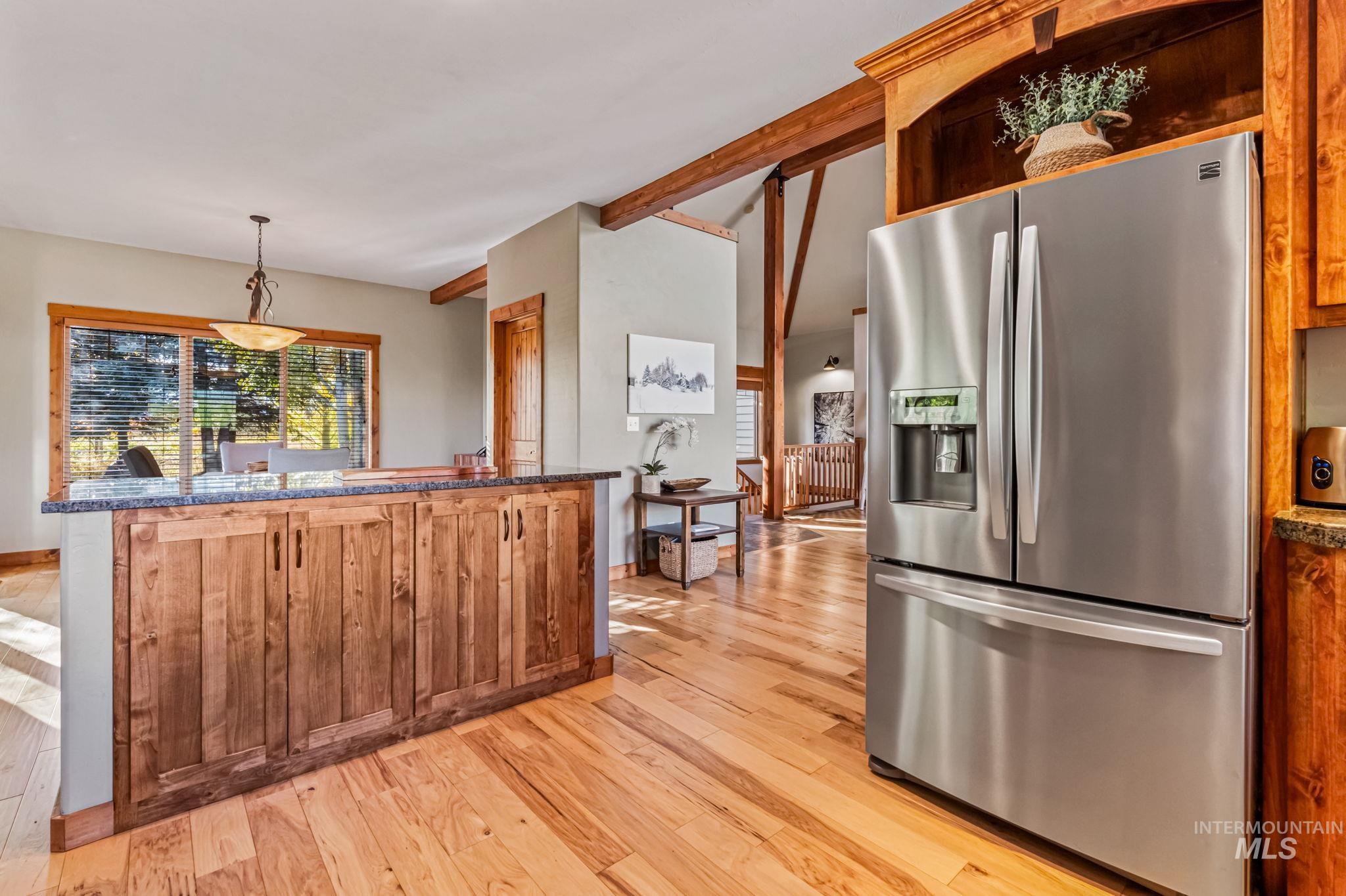Kitchen featuring stainless steel fridge, decorative light fixtures, dark stone counters, light wood finished floors, and beamed ceiling