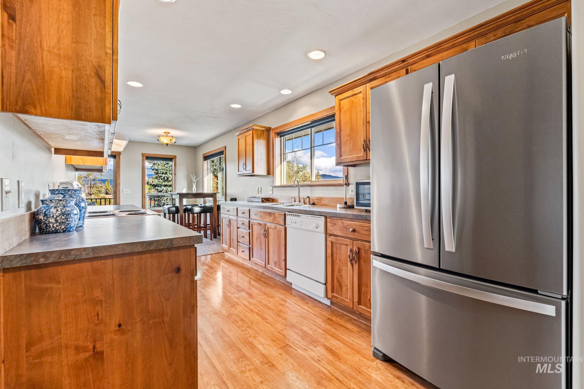 Kitchen featuring freestanding refrigerator, recessed lighting, light wood finished floors, brown cabinetry, and dishwasher