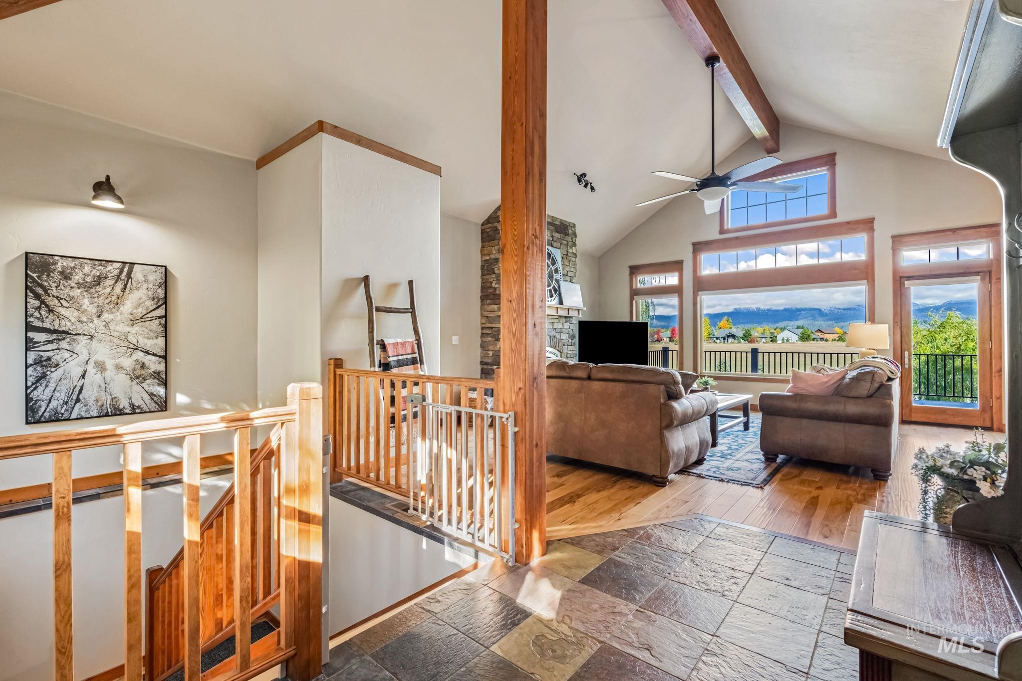 Living area with beamed ceiling, high vaulted ceiling, stone tile flooring, and ceiling fan