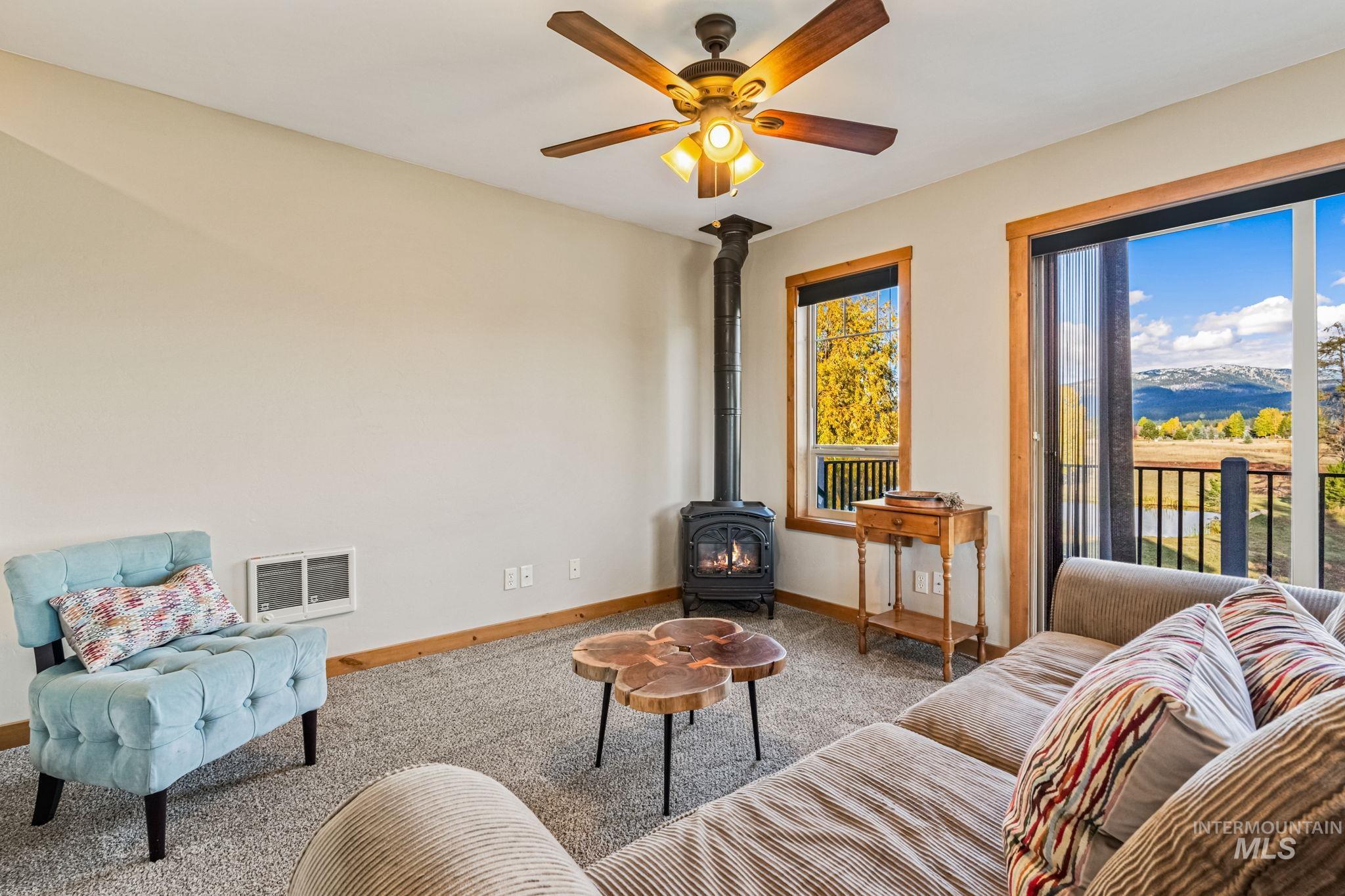 Living area with a wood stove, carpet floors, and ceiling fan