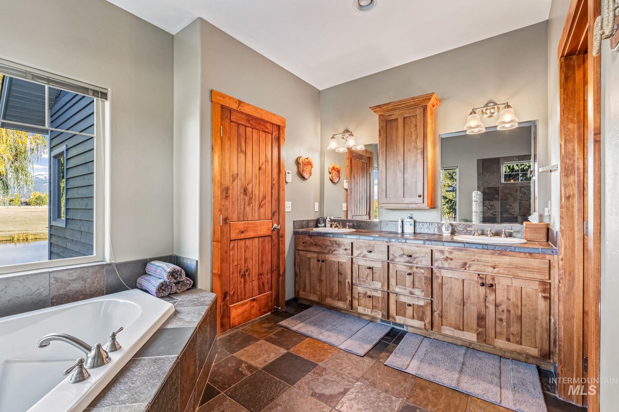 Bathroom featuring double vanity, stone tile flooring, and a bath