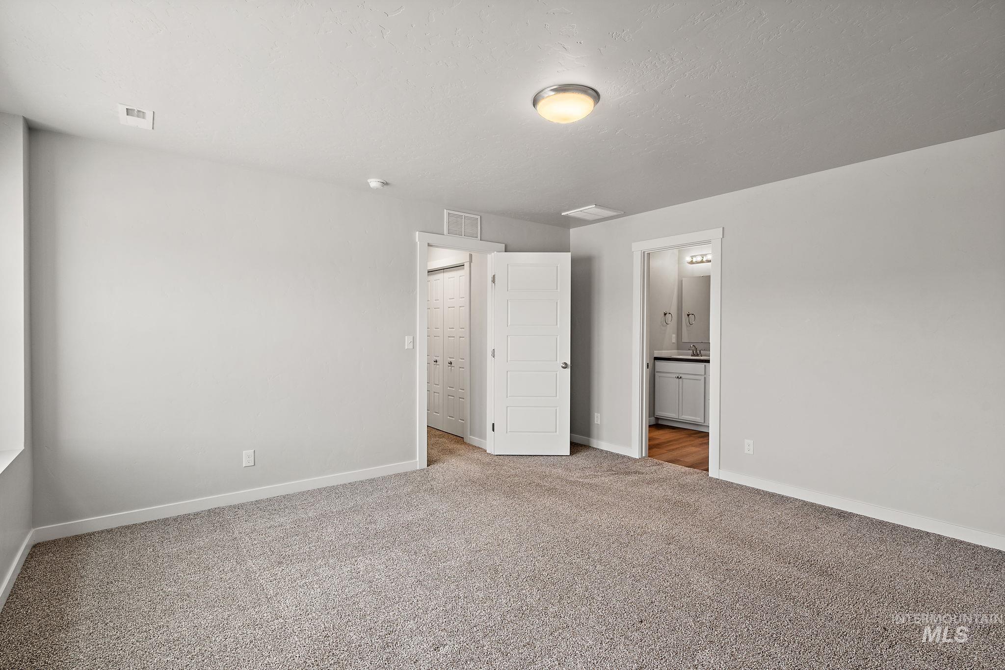 Unfurnished bedroom featuring light carpet, a textured ceiling, and ensuite bathroom