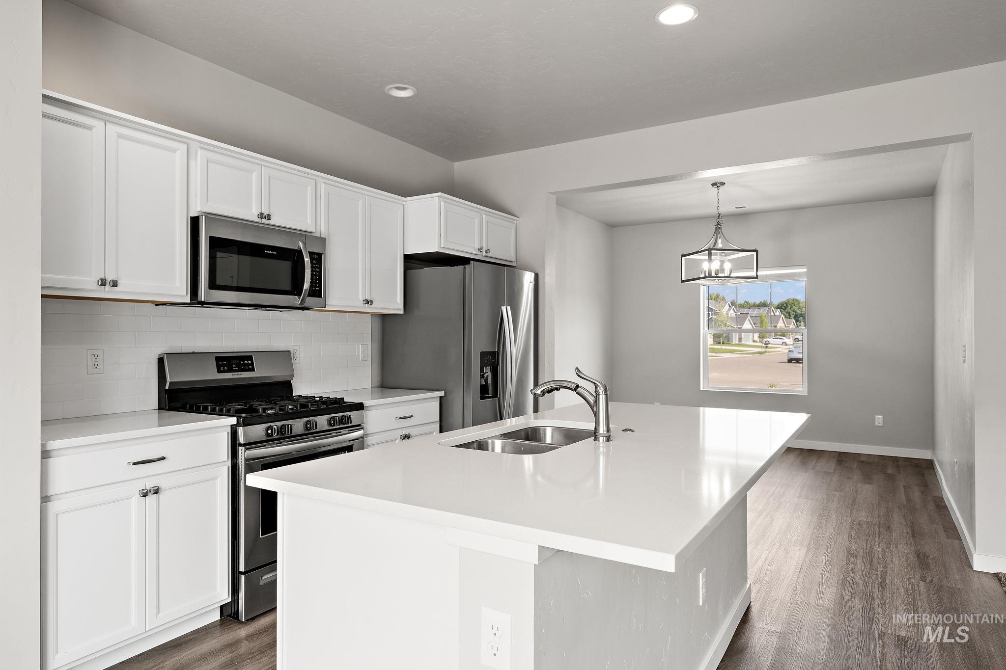 Kitchen featuring appliances with stainless steel finishes, white cabinetry, a center island with sink, dark wood-style floors, and pendant lighting