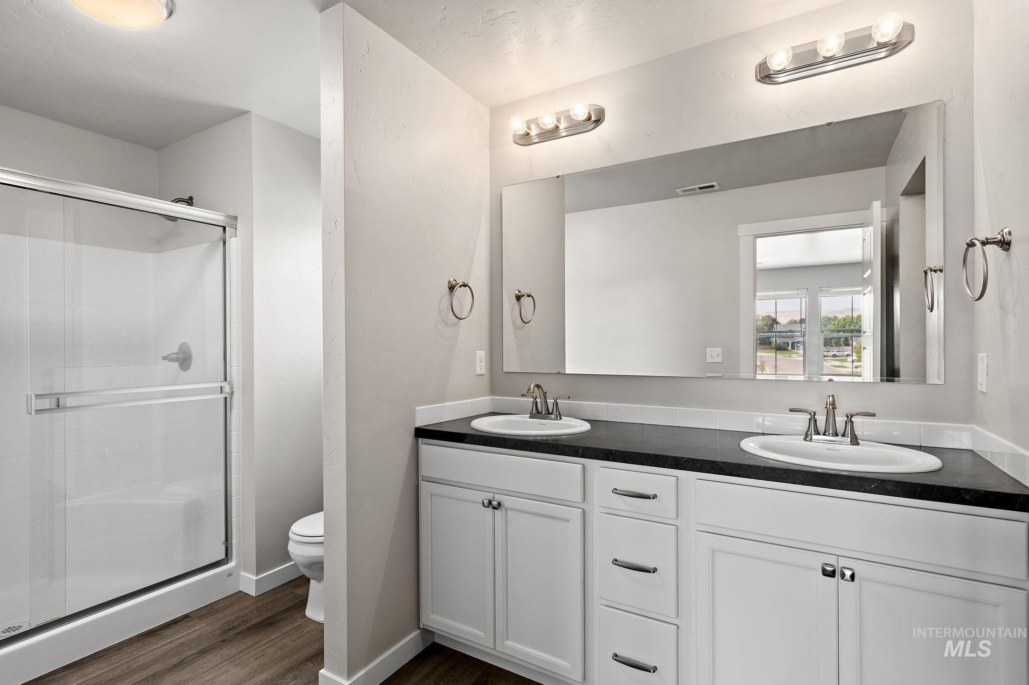 Full bath featuring double vanity, a shower stall, and dark wood-style flooring