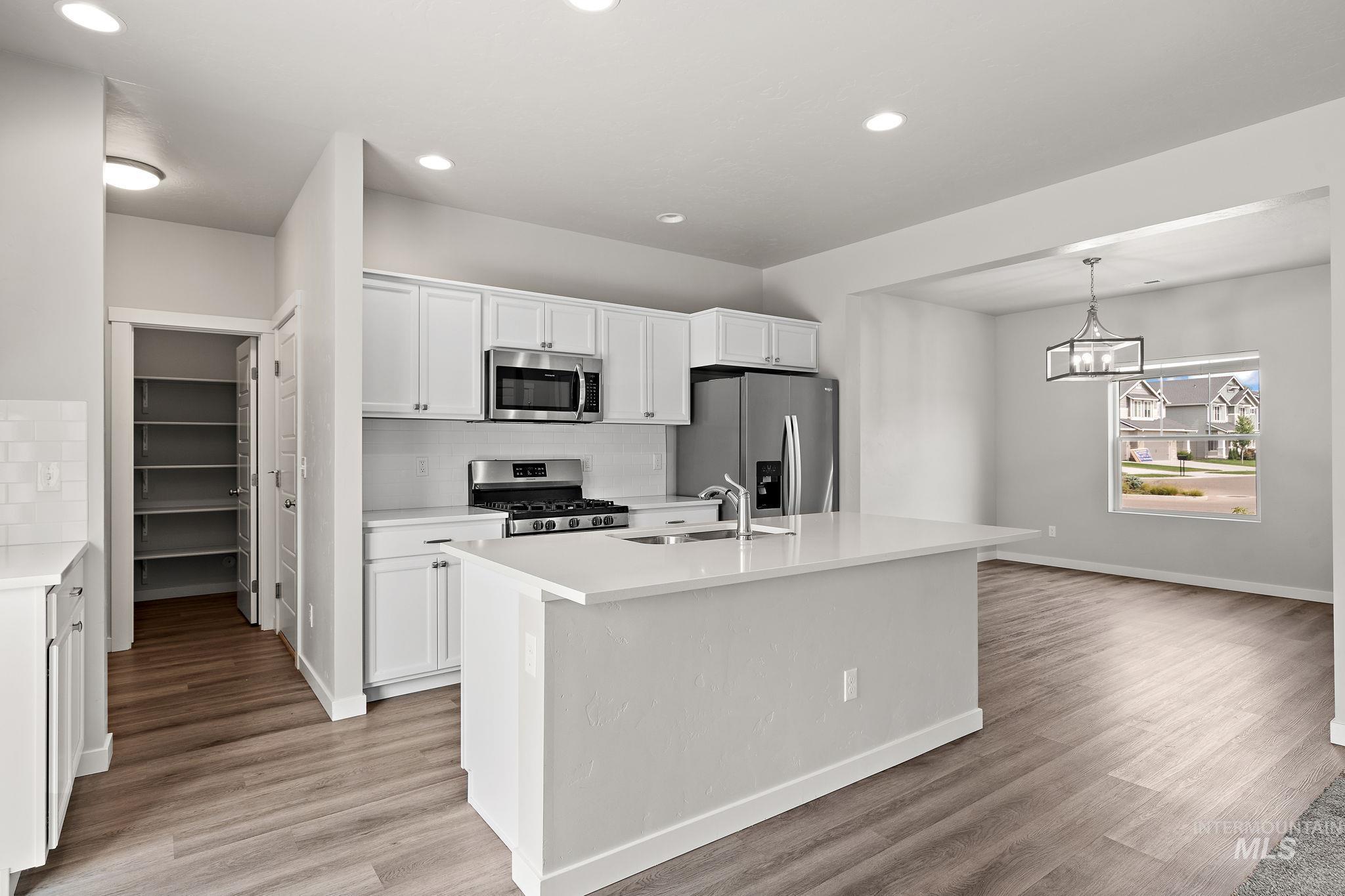 Kitchen featuring decorative backsplash, stainless steel appliances, a center island with sink, white cabinetry, and hanging light fixtures