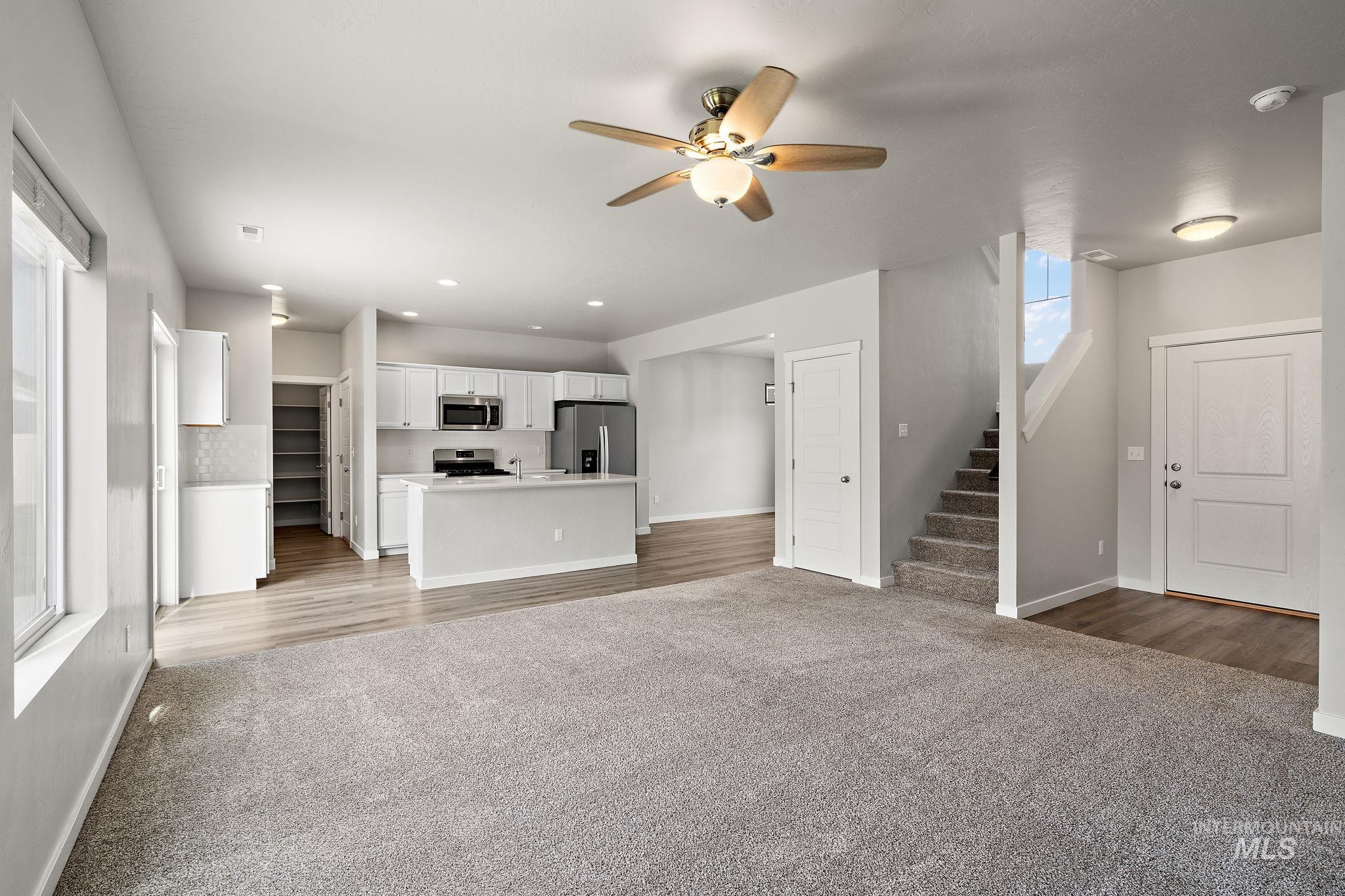Unfurnished living room featuring light colored carpet, a ceiling fan, stairway, and recessed lighting