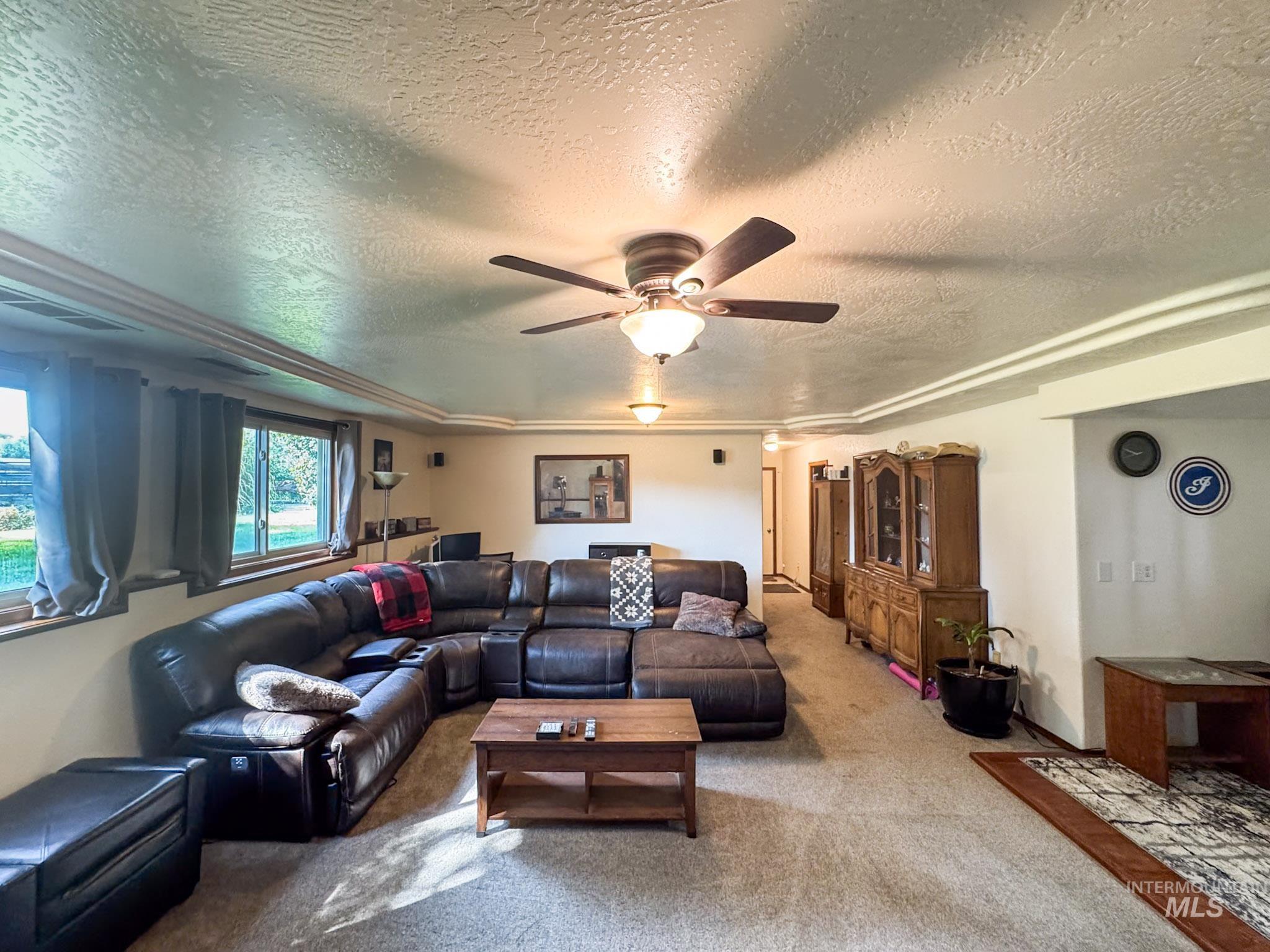 Carpeted living room with a textured ceiling and ceiling fan