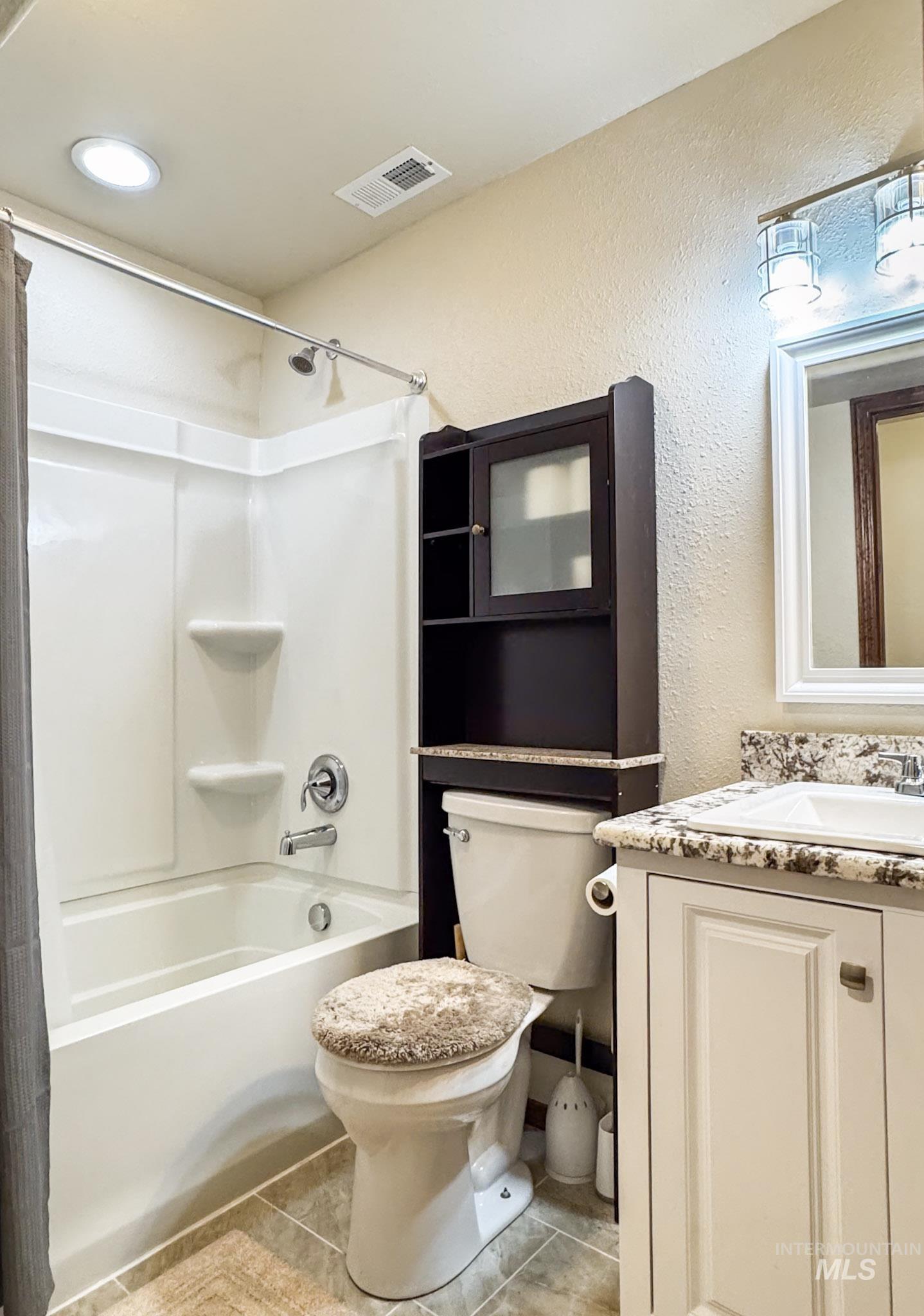 Full bathroom with light tile patterned floors, shower / bath combo, vanity, and a textured wall