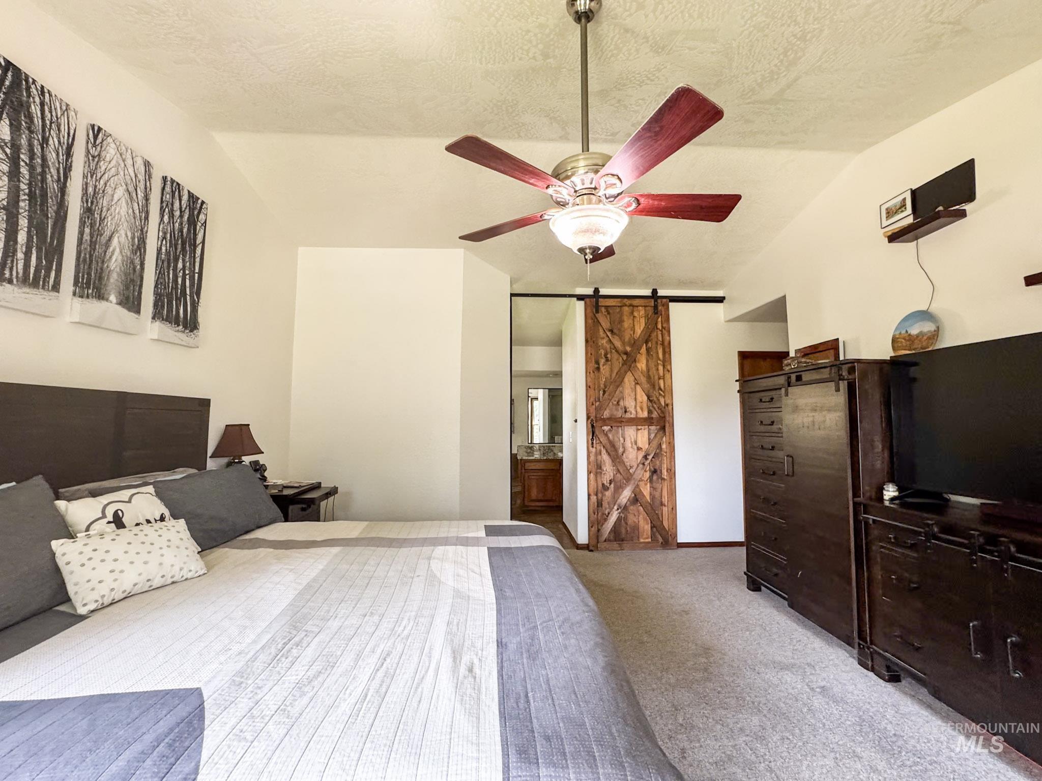 Carpeted bedroom featuring a barn door, a textured ceiling, ensuite bath, ceiling fan, and lofted ceiling