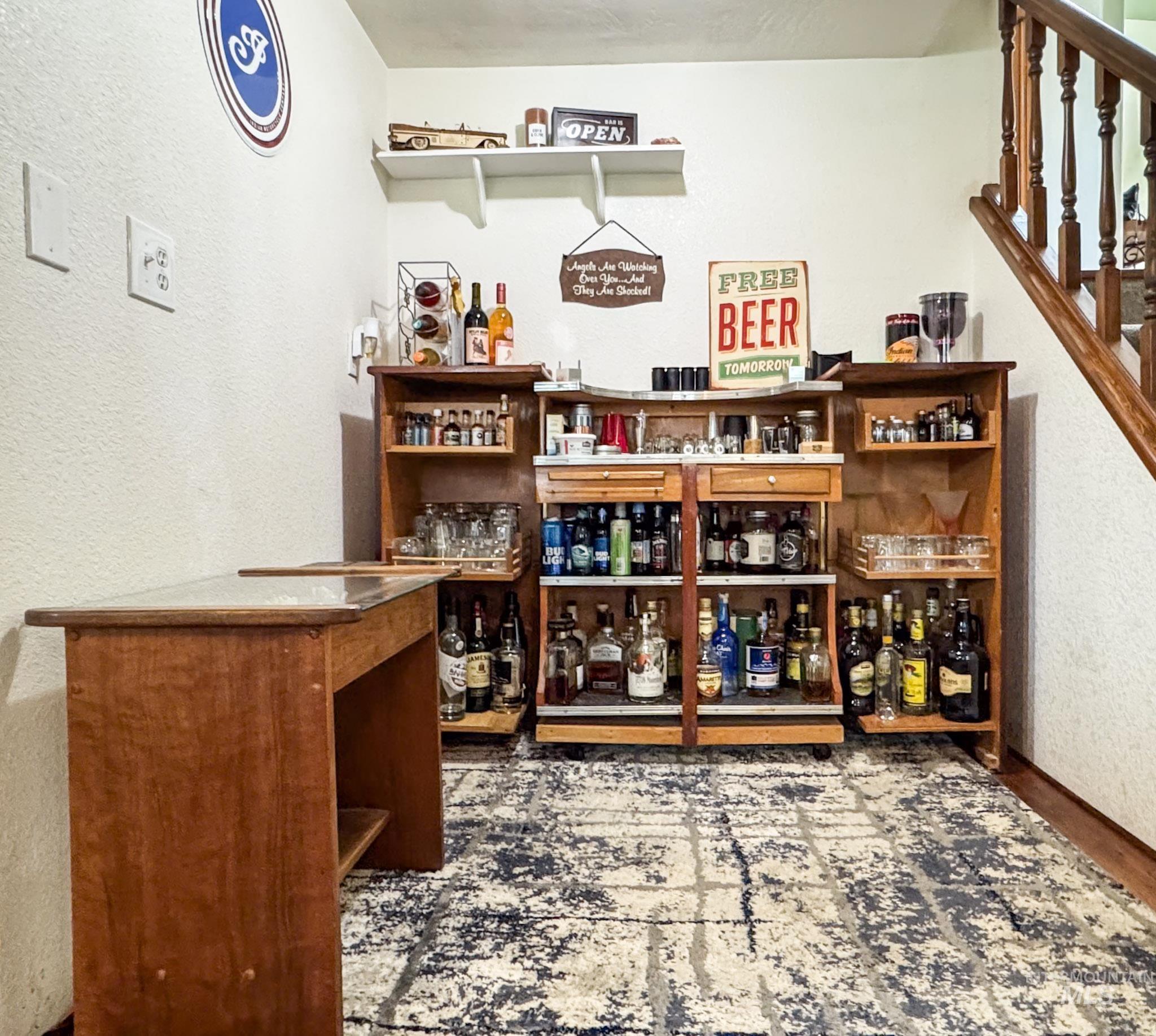Indoor dry bar featuring a textured wall, open shelves, stairway, and light wood-type flooring