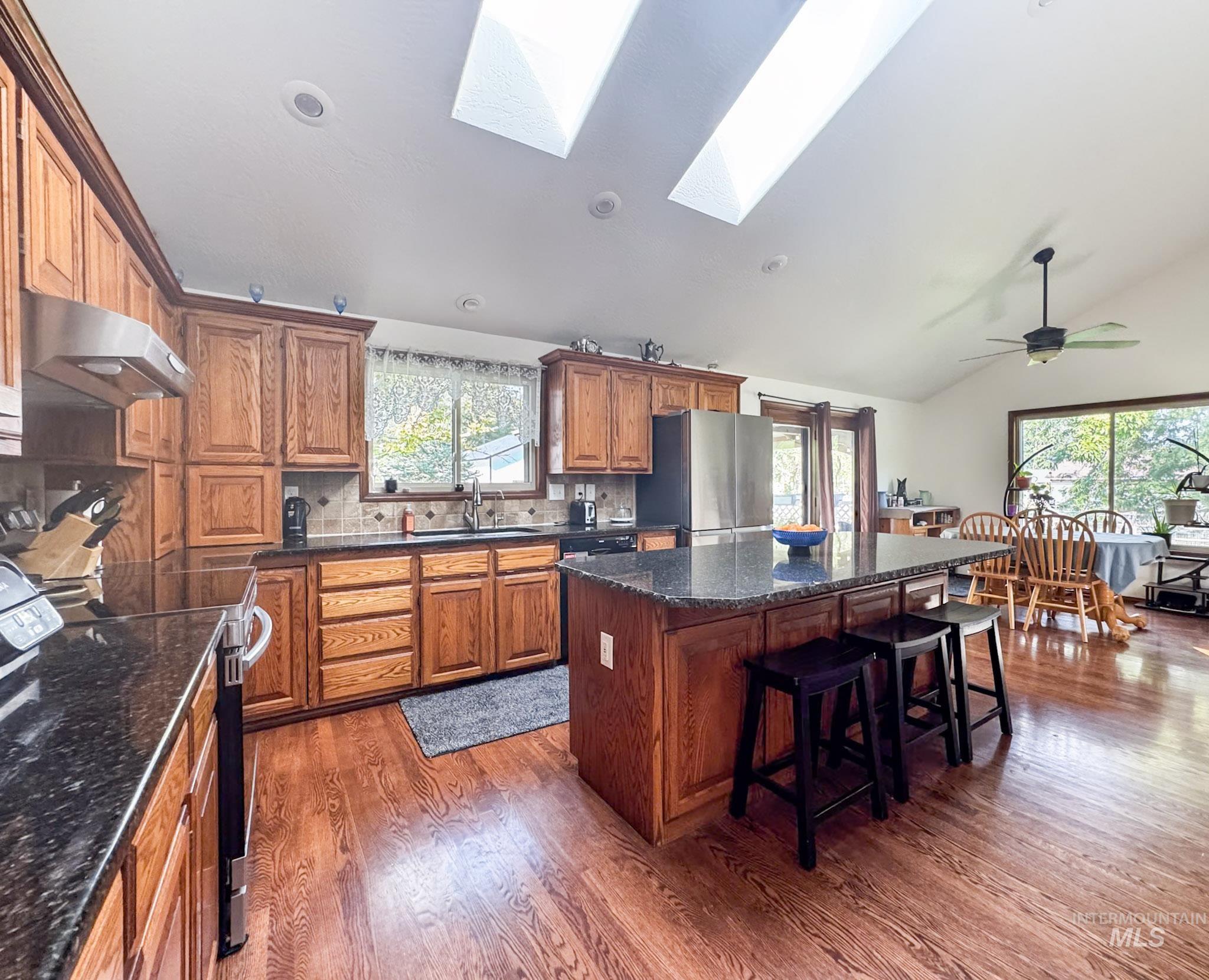 Kitchen with backsplash, black electric range oven, dark stone countertops, brown cabinets, and lofted ceiling