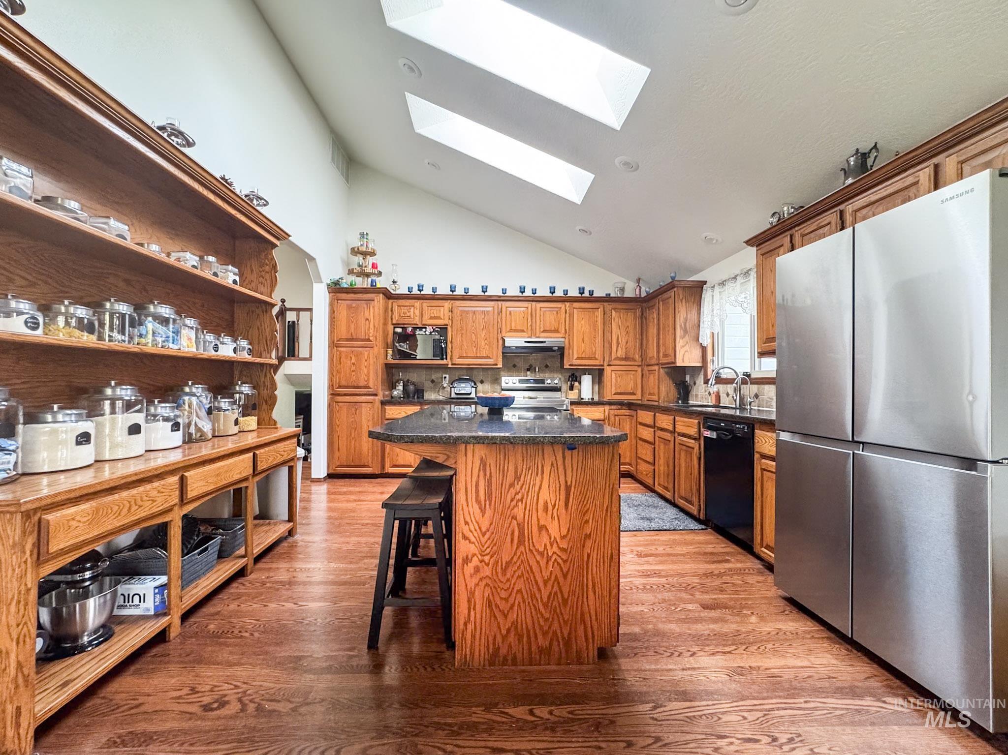 Kitchen with stainless steel appliances, a breakfast bar area, a center island, dark wood finished floors, and a skylight