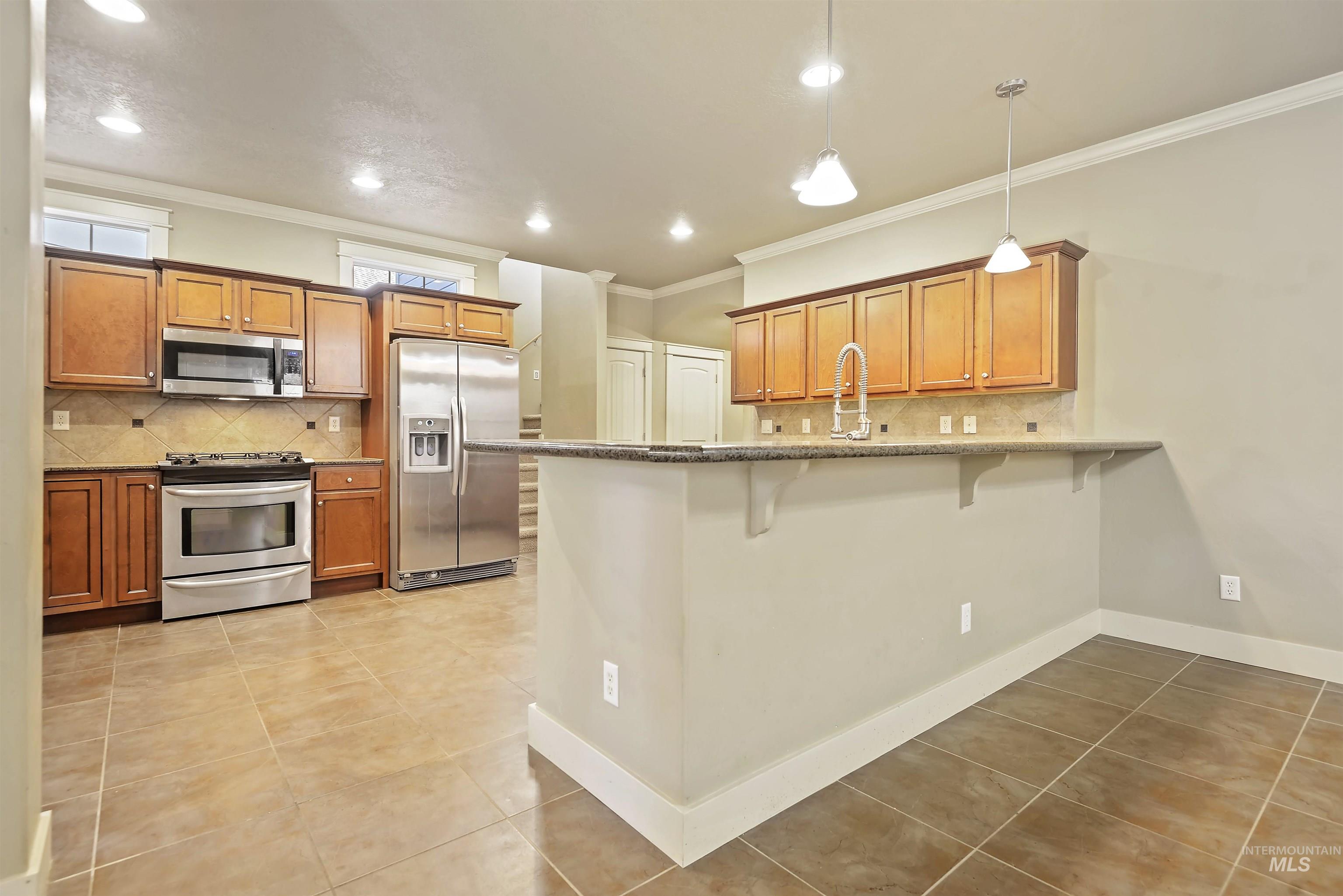 Kitchen with tasteful backsplash, brown cabinets, appliances with stainless steel finishes, light tile patterned flooring, and a peninsula