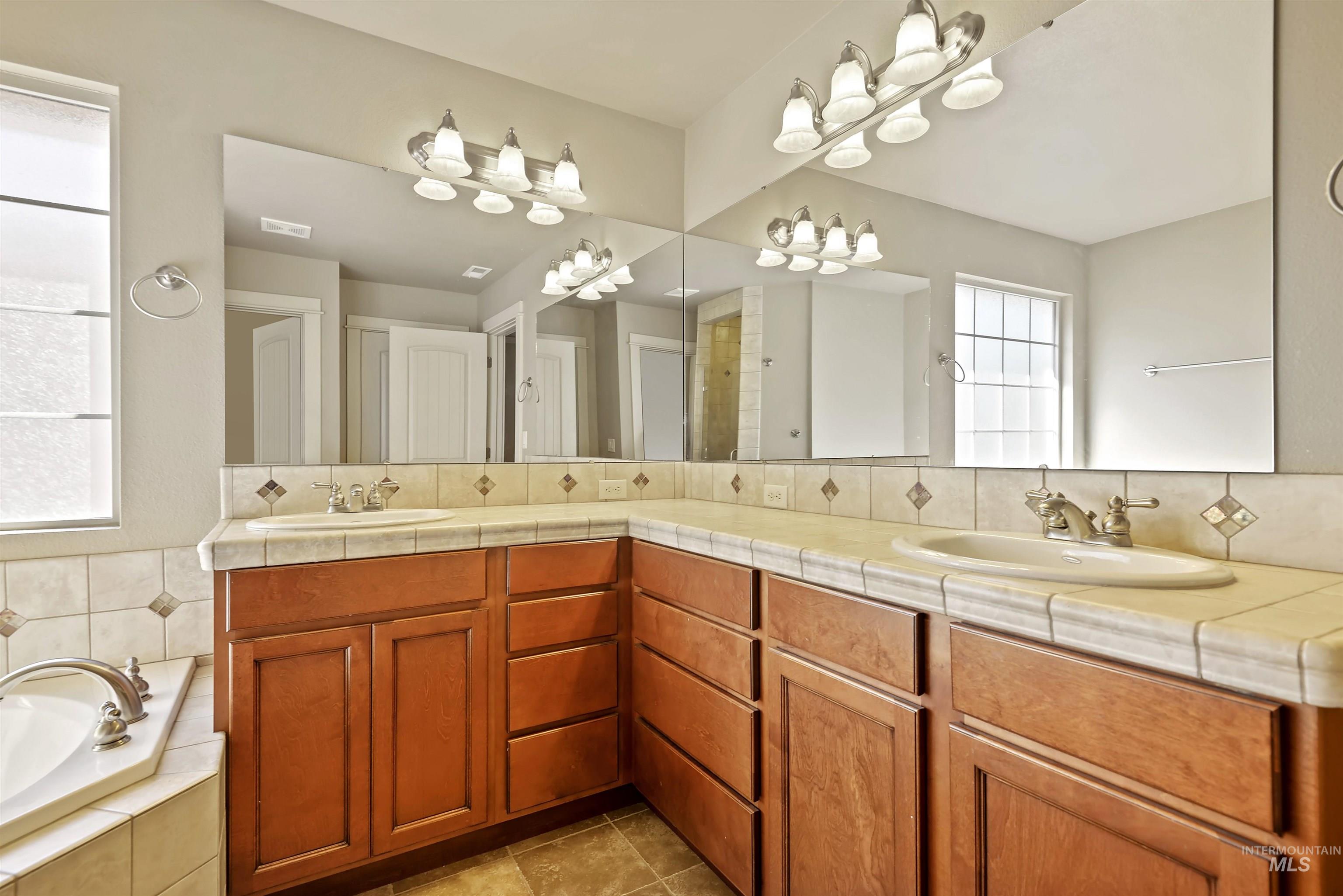 Full bath featuring double vanity, a garden tub, light tile patterned flooring, and backsplash
