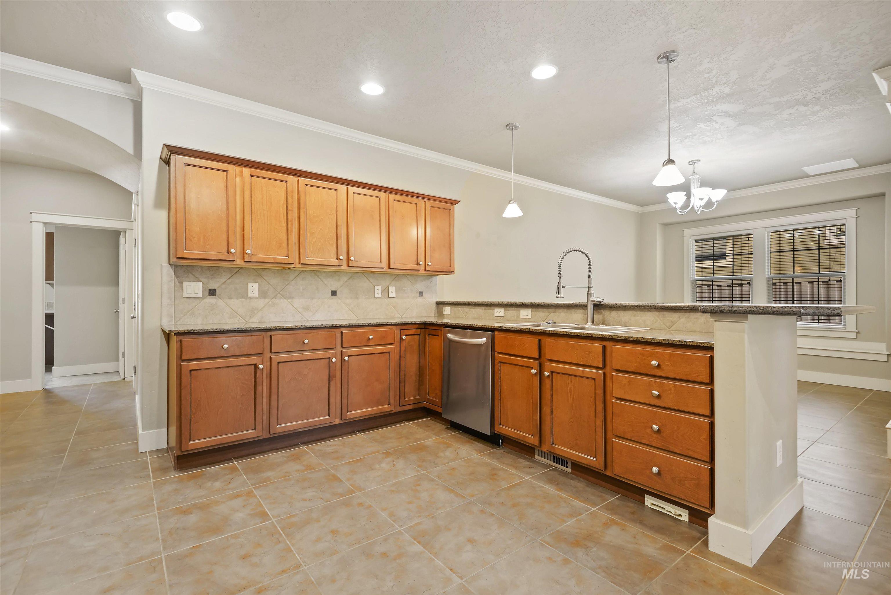 Kitchen with brown cabinetry, light tile patterned flooring, ornamental molding, decorative backsplash, and pendant lighting