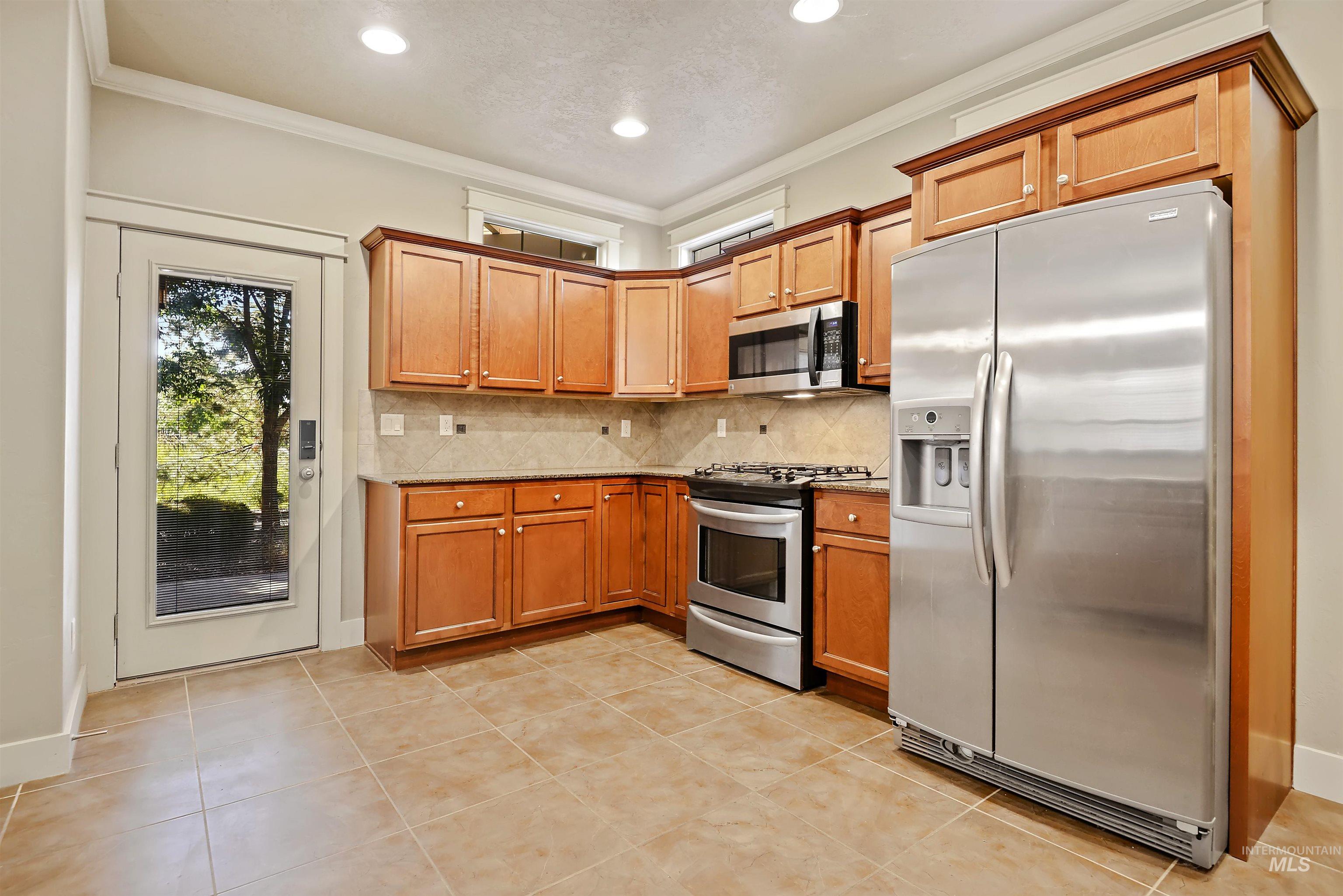 Kitchen with stainless steel appliances, crown molding, tasteful backsplash, light tile patterned flooring, and brown cabinets