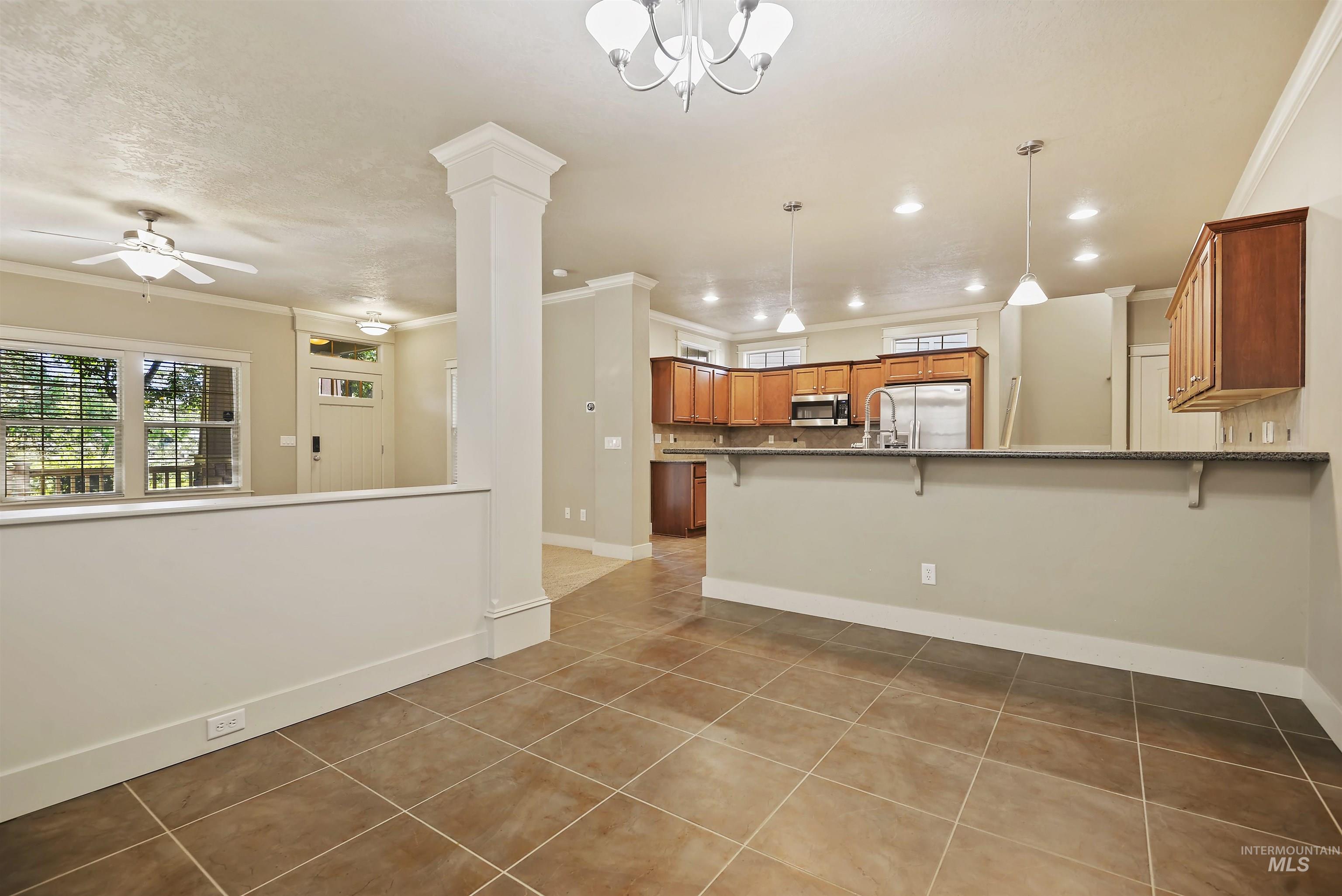 Kitchen with a breakfast bar area, light tile patterned floors, ornamental molding, brown cabinetry, and stainless steel appliances