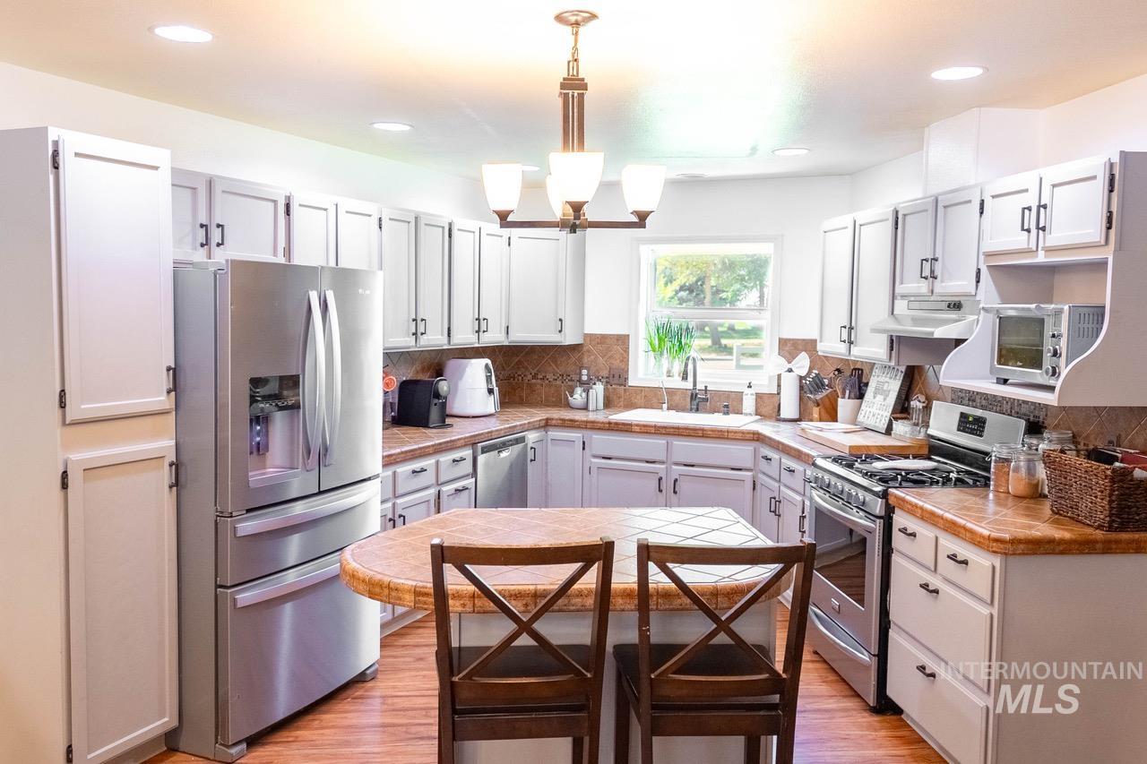 Kitchen with appliances with stainless steel finishes, light wood-style flooring, pendant lighting, tasteful backsplash, and recessed lighting