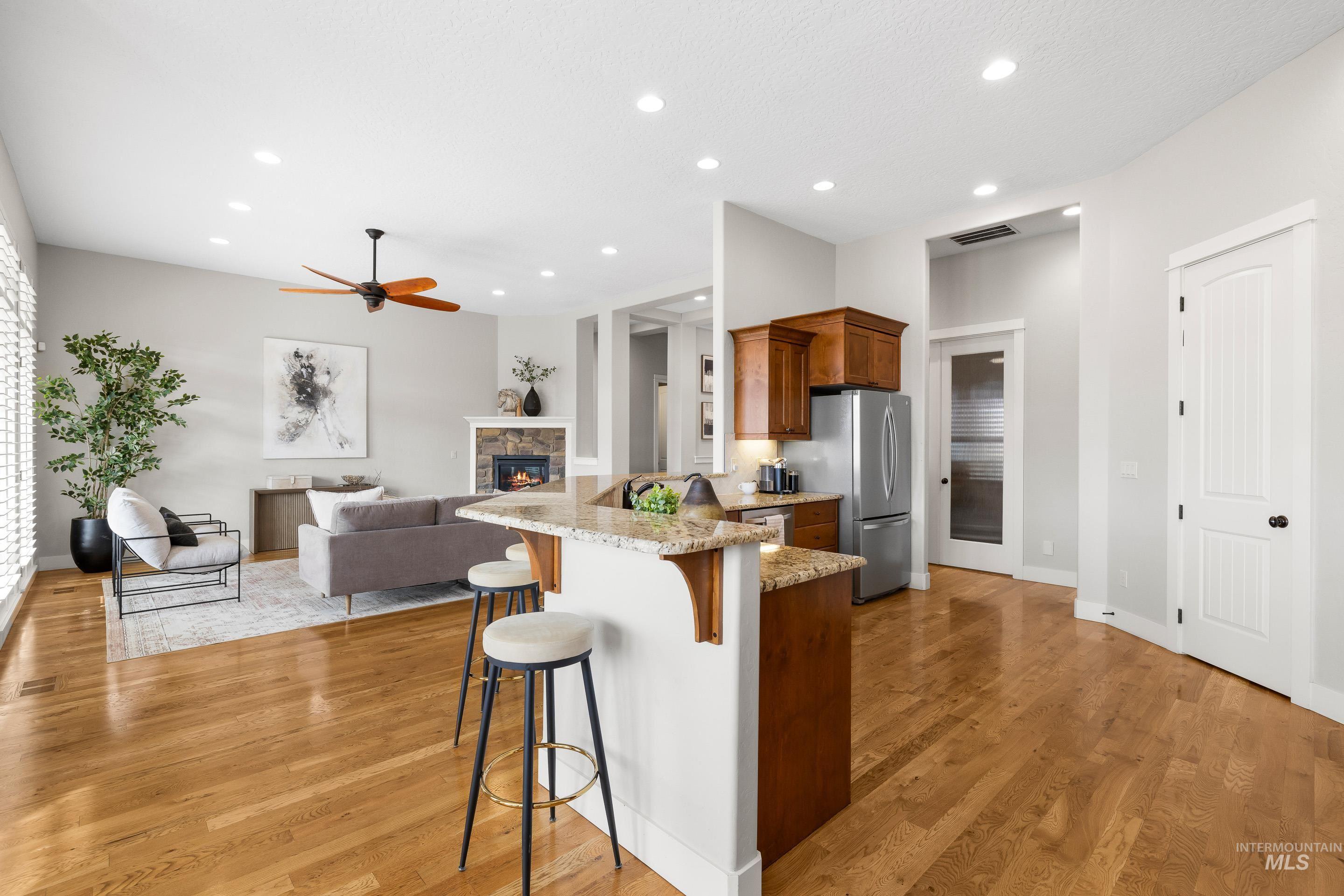 Kitchen with a kitchen bar, light stone countertops, brown cabinets, a stone fireplace, and a peninsula