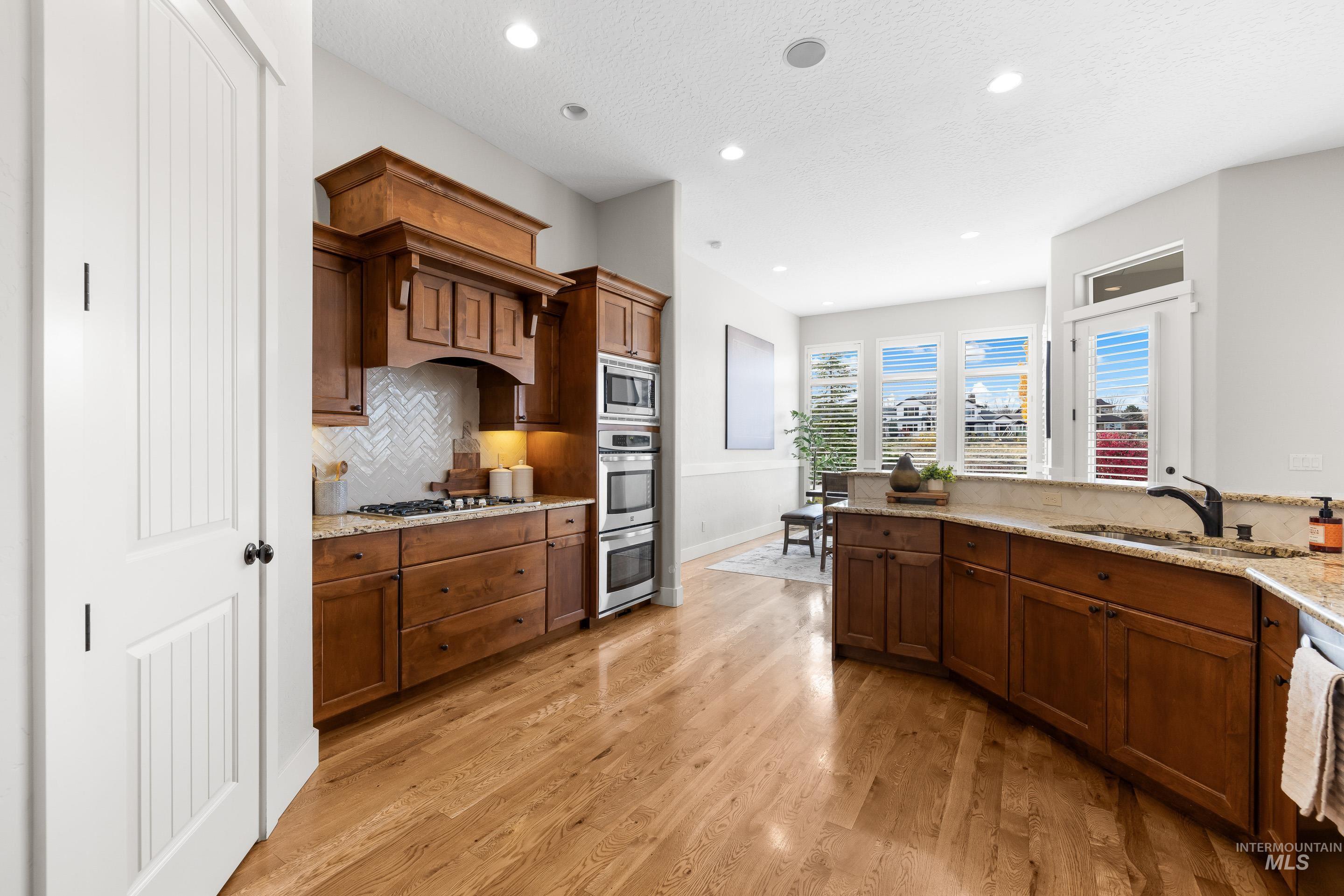 Kitchen with light stone counters, decorative backsplash, recessed lighting, light wood-style floors, and brown cabinetry