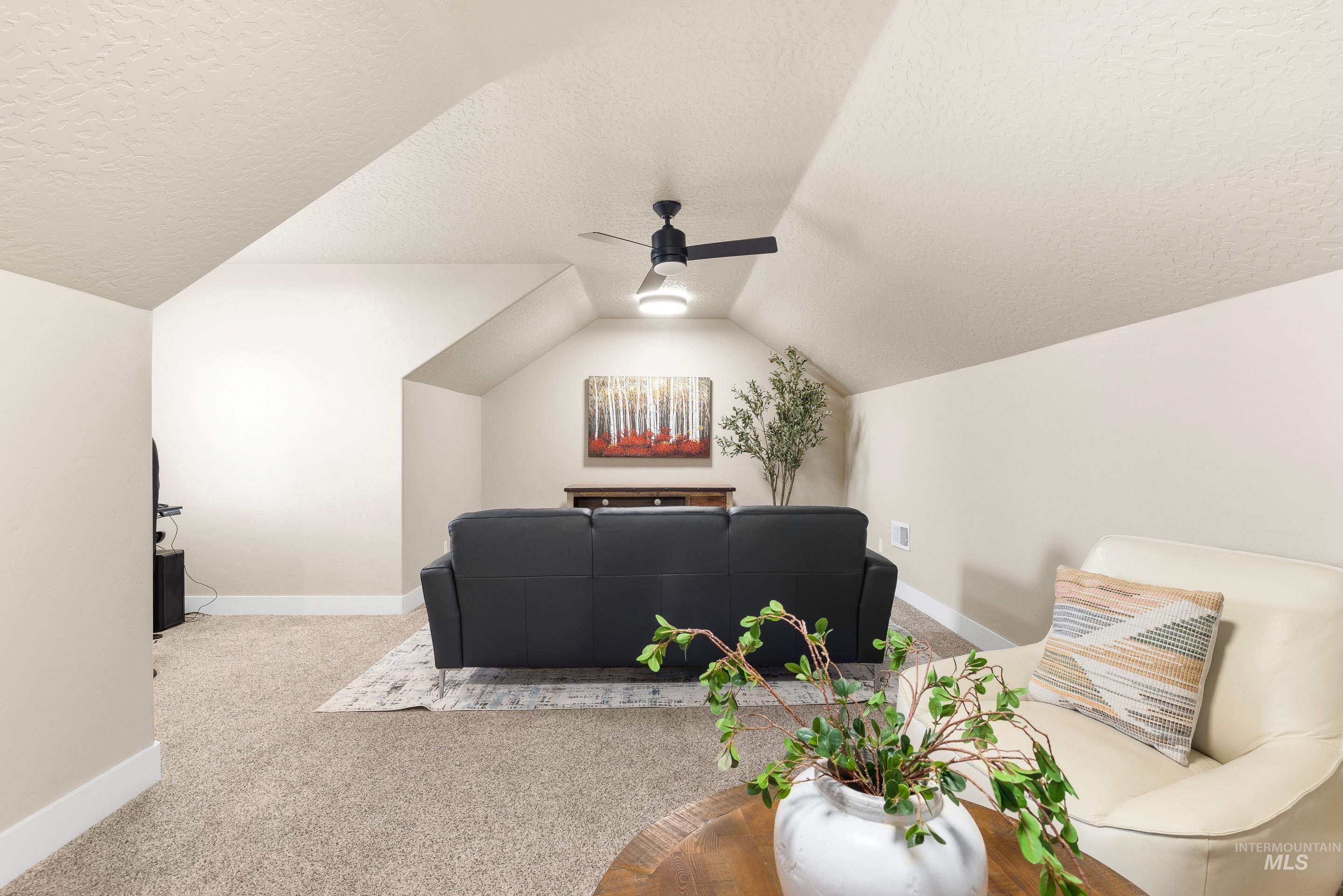 Carpeted home theater featuring a textured ceiling, vaulted ceiling, and ceiling fan