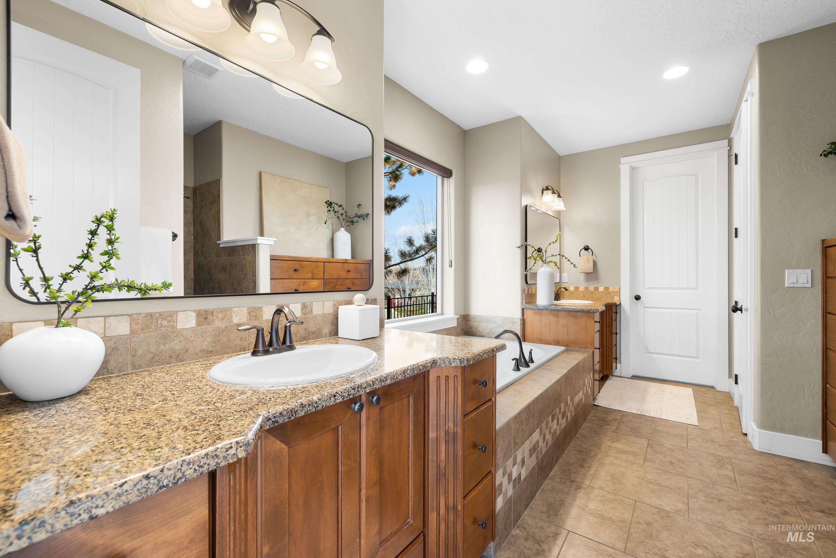 Full bath with two vanities, light tile patterned floors, recessed lighting, and a relaxing tiled tub