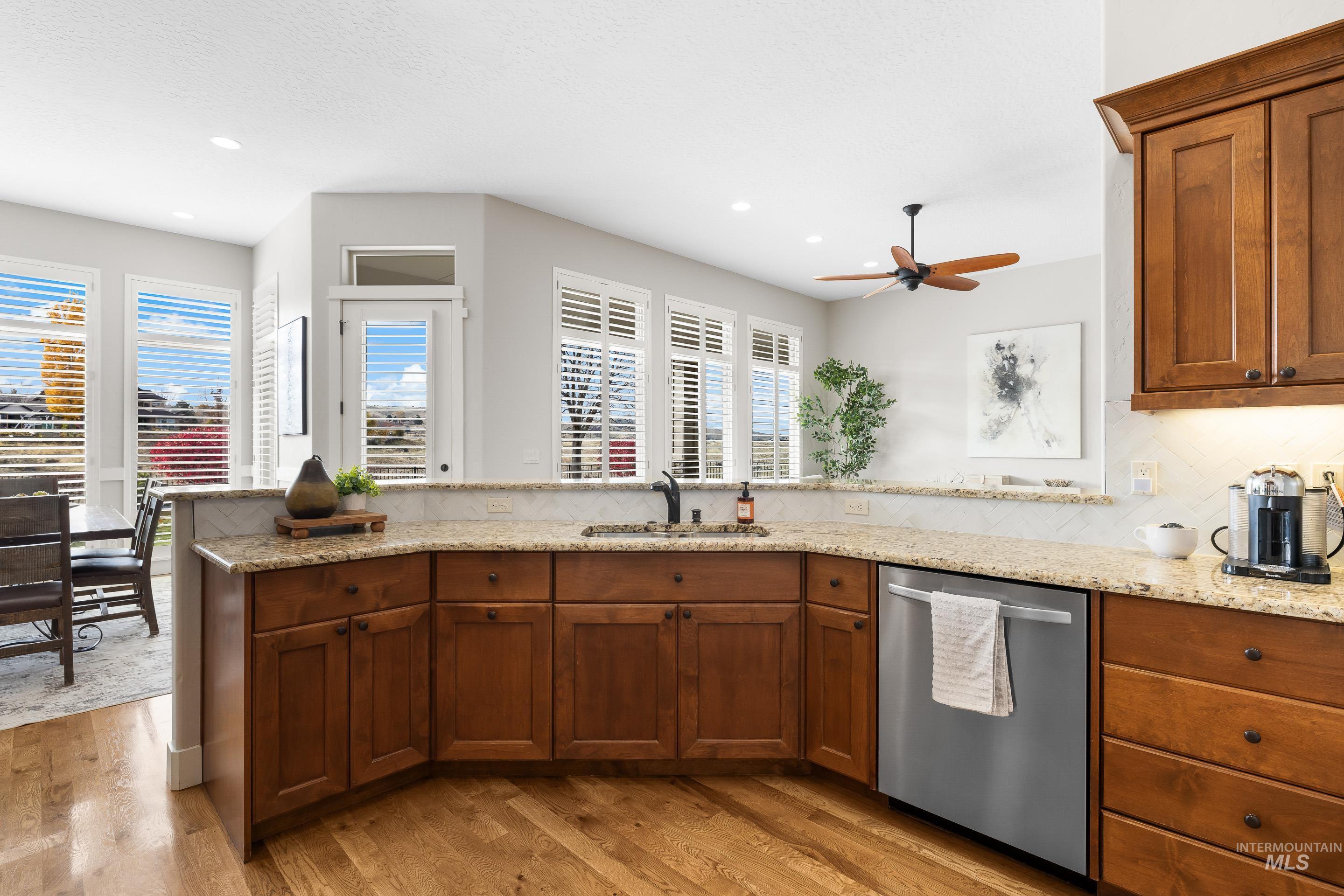 Kitchen featuring brown cabinetry, stainless steel dishwasher, light stone countertops, light wood-style floors, and backsplash