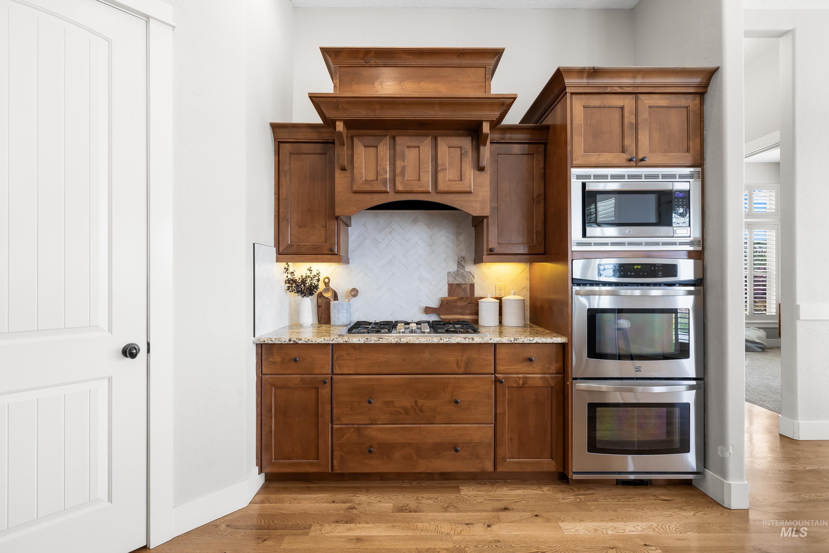 Kitchen with tasteful backsplash, brown cabinets, stainless steel appliances, light wood-type flooring, and light stone counters