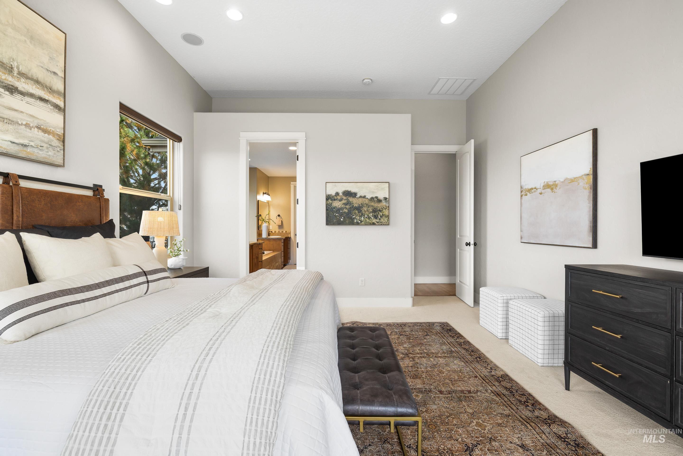 Bedroom with light colored carpet, recessed lighting, and connected bathroom