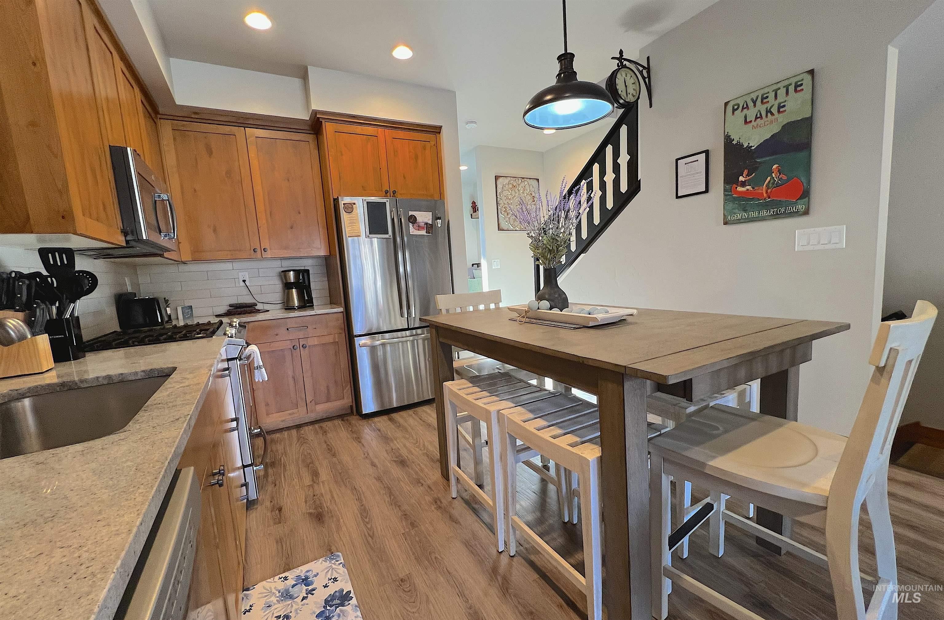 Kitchen featuring brown cabinets, appliances with stainless steel finishes, tasteful backsplash, light wood-type flooring, and hanging light fixtures